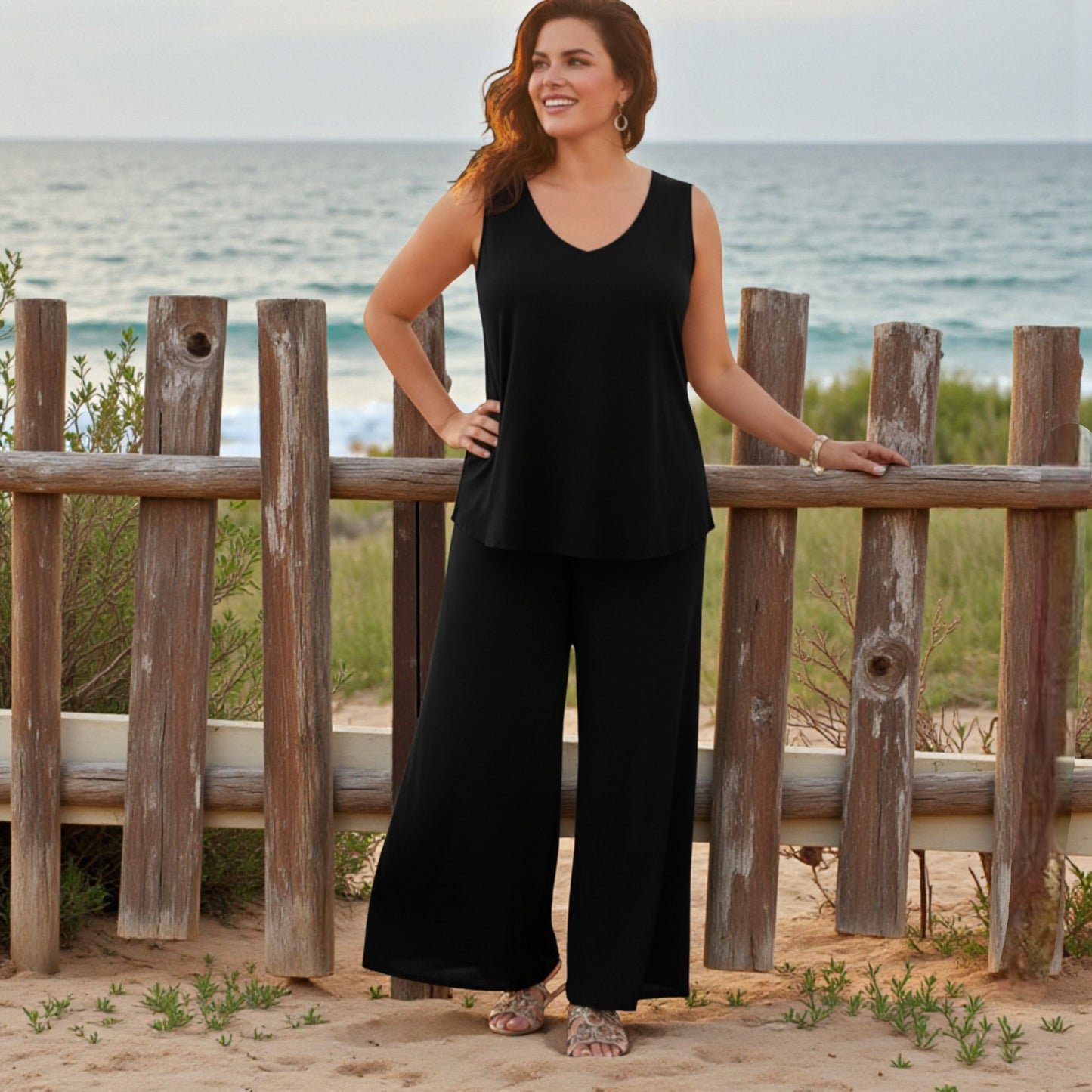 Woman in black outfit standing by a wooden fence with ocean view