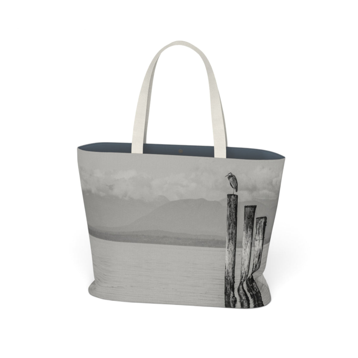 A tote bag featuring a grayscale landscape print of a lake, mountains, and wooden posts with a bird, complete with light beige fabric handles, shown on a plain white background.