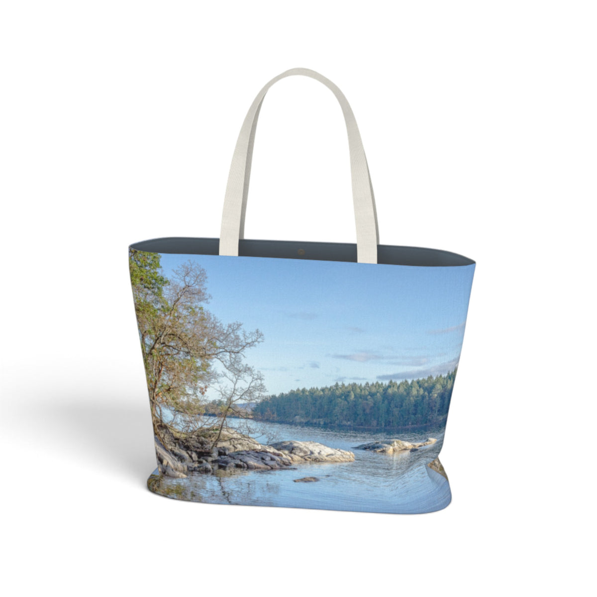 A tote bag featuring a scenic landscape print of a rocky river, trees, and blue sky, with light beige shoulder straps, shown on a white background.