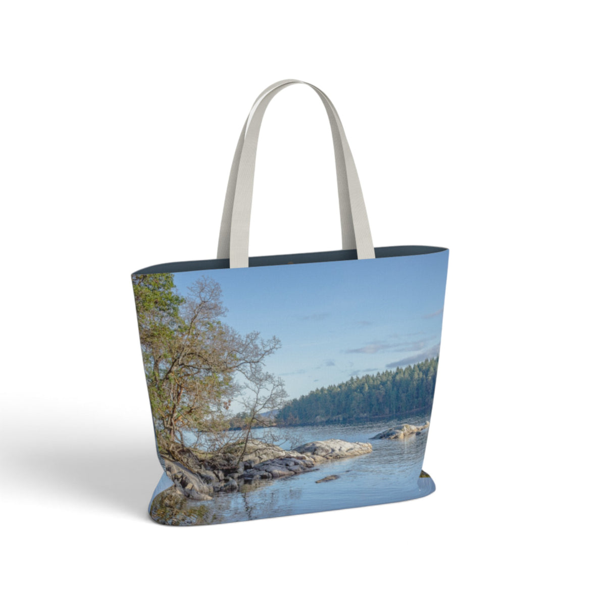 A tote bag featuring a scenic landscape print of a rocky river bend with trees under a blue sky, complete with light gray fabric shoulder straps, shown on a white background.