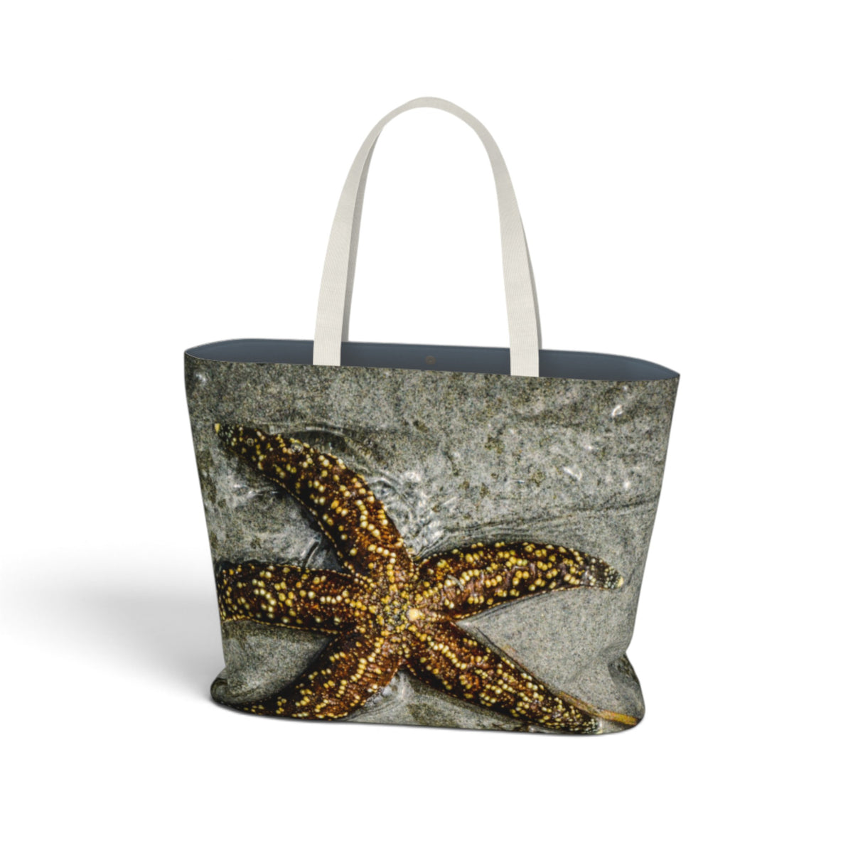 A tote bag featuring a realistic print of a golden-brown starfish on a gray textured background, with white shoulder straps, shown on a plain white background.