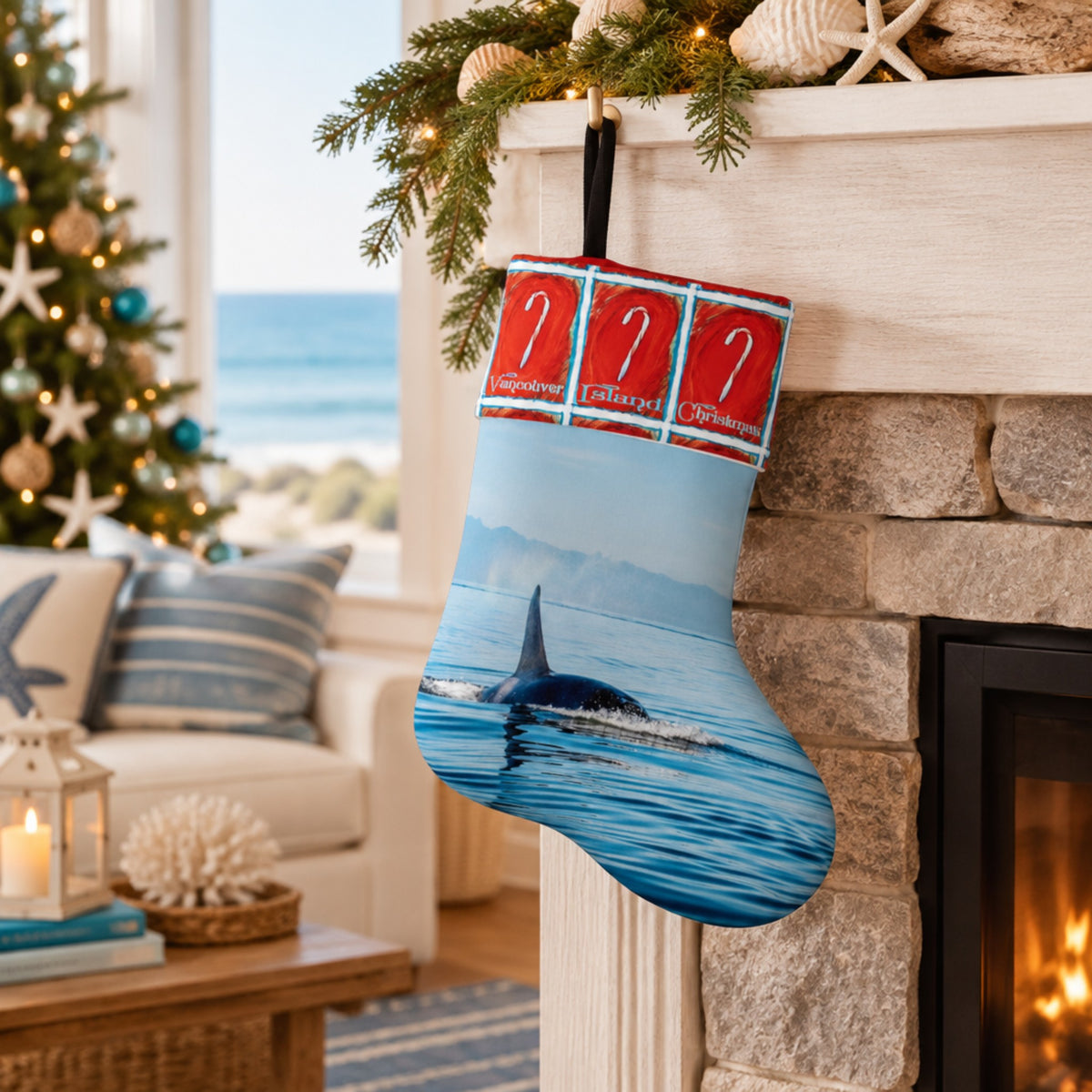 A Christmas stocking with a blue orca whale print hangs from a fireplace mantel decorated with pine branches and starfish, with a cozy living room and ocean view in the background.