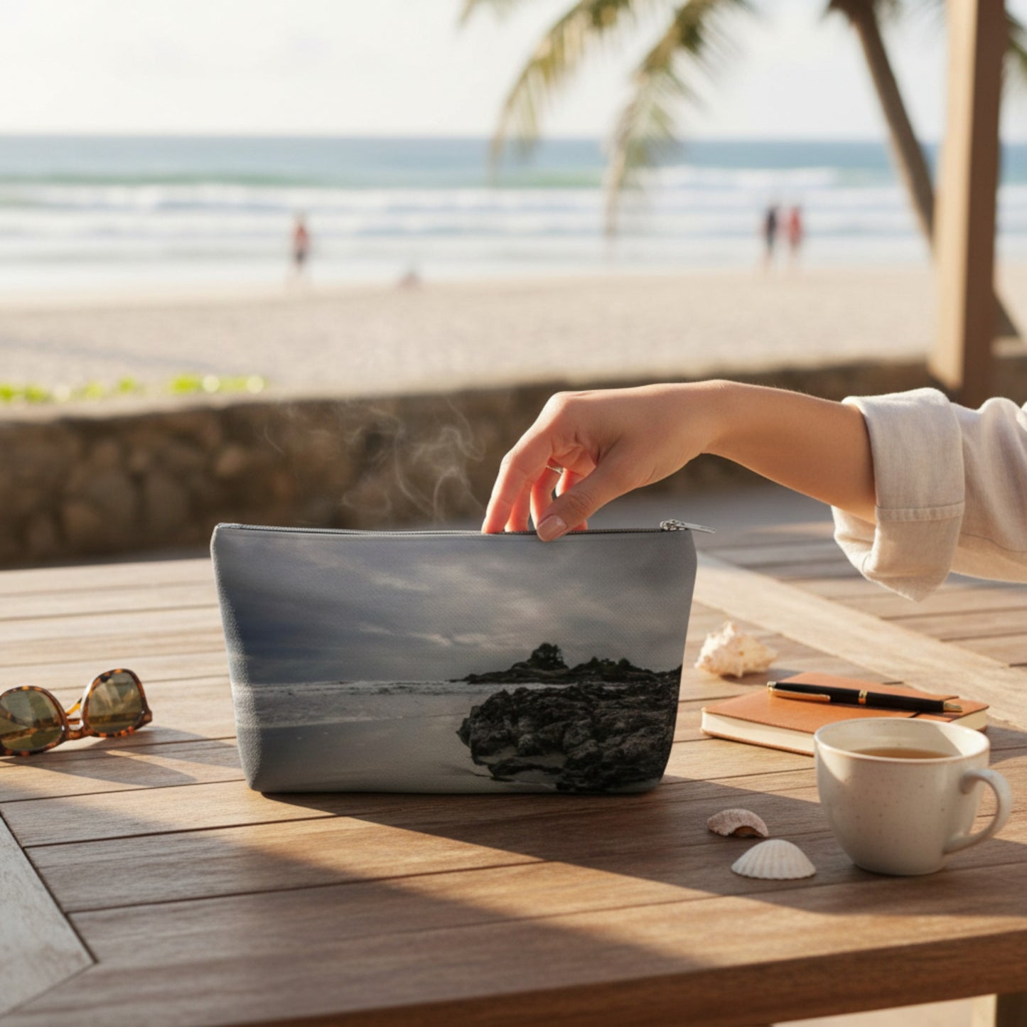 Hand opening a pouch with a beach design on a wooden table by the sea.