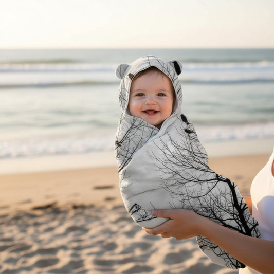 Baby wrapped in a tree-patterned swaddle on a beach