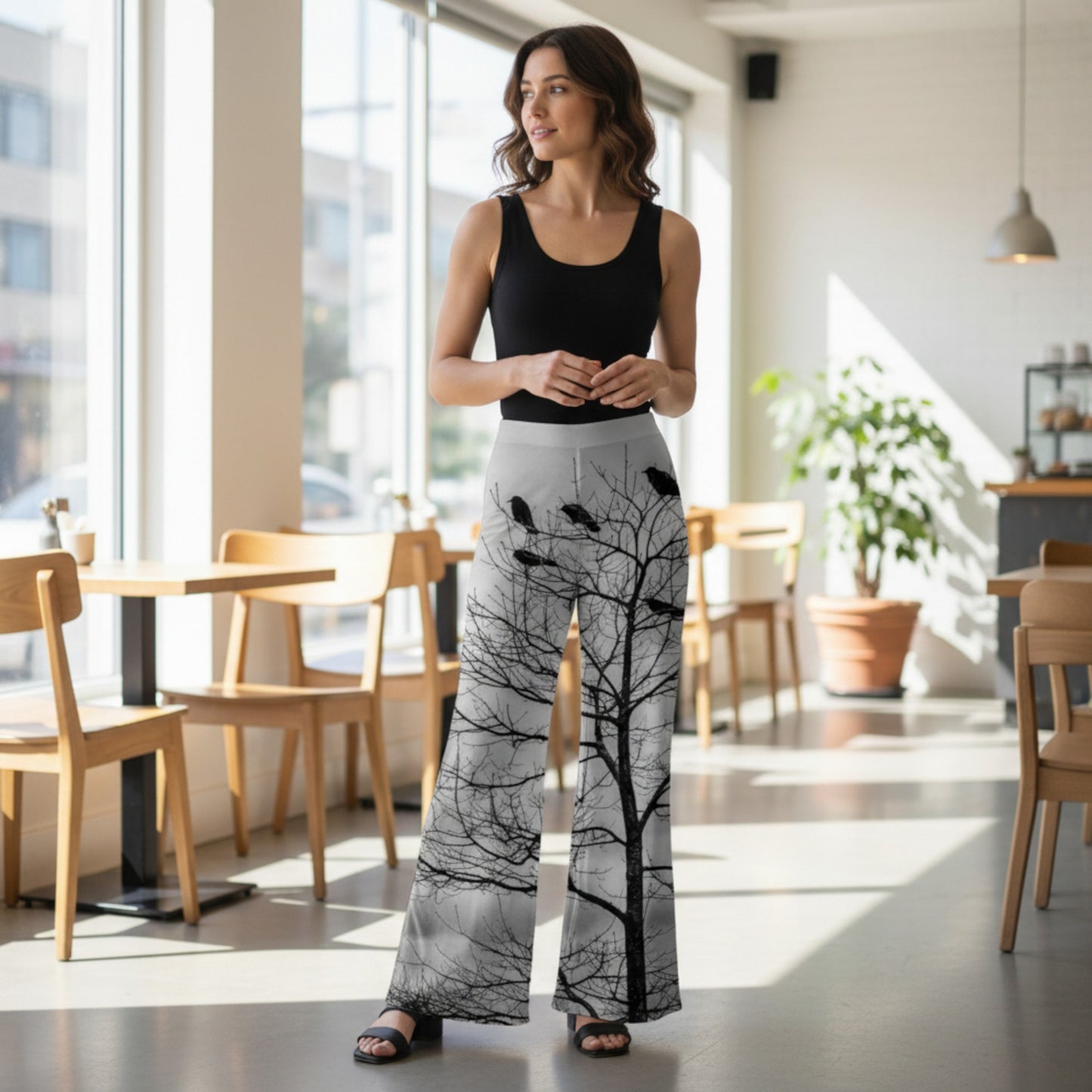 Woman wearing a black tank top and white pants with black tree pattern in a modern cafe.