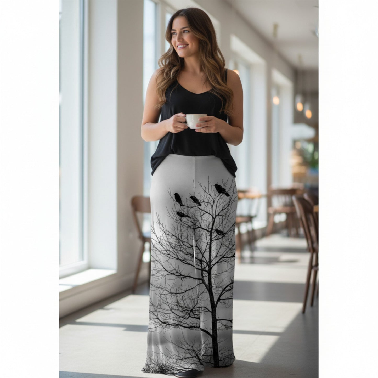 Woman wearing a black and white dress with tree and bird design, holding a cup indoors.