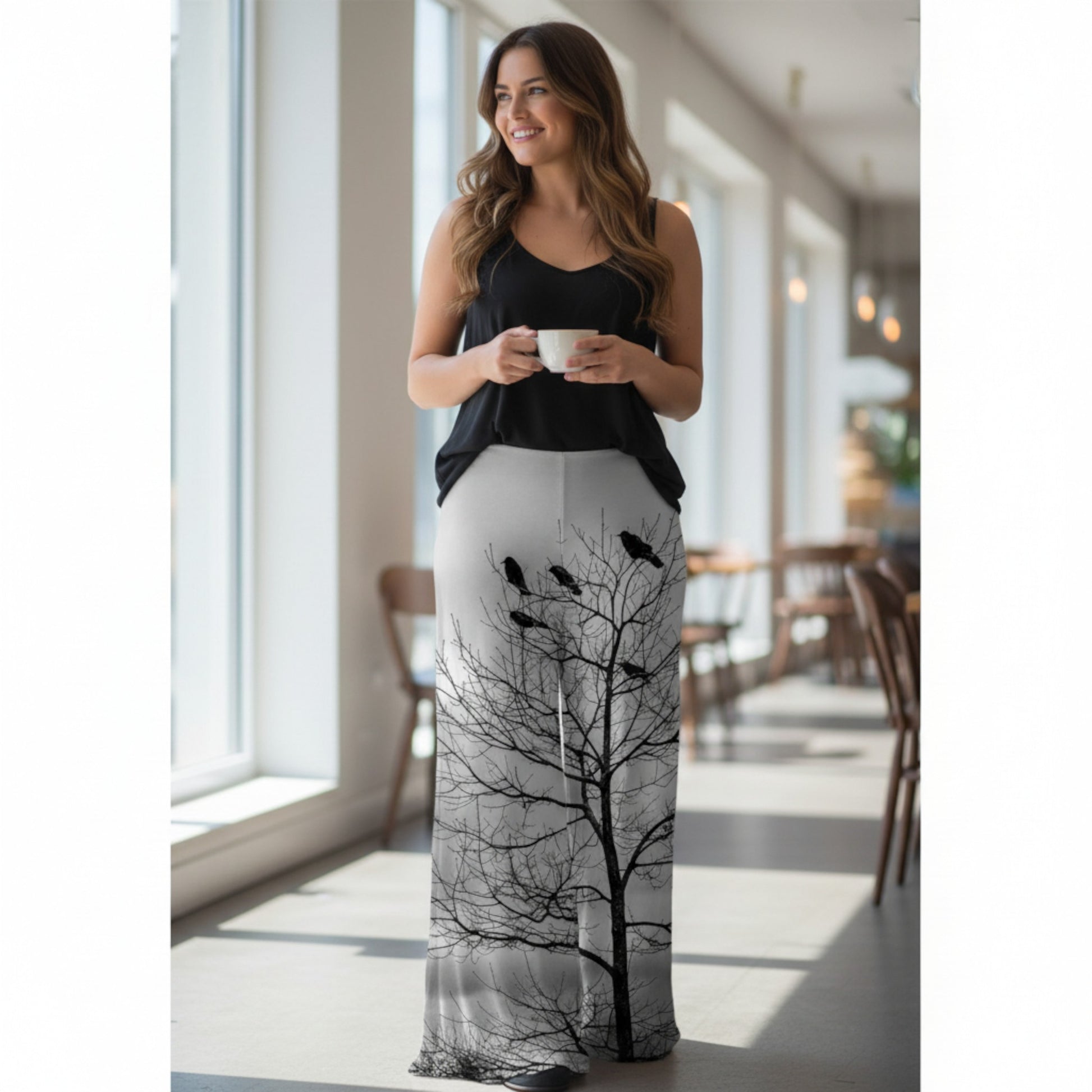 Woman wearing a black and white dress with tree and bird design, holding a cup indoors.