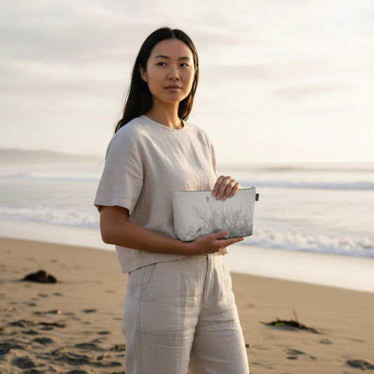 Woman holding a nature-patterned clutch on a beach at sunset