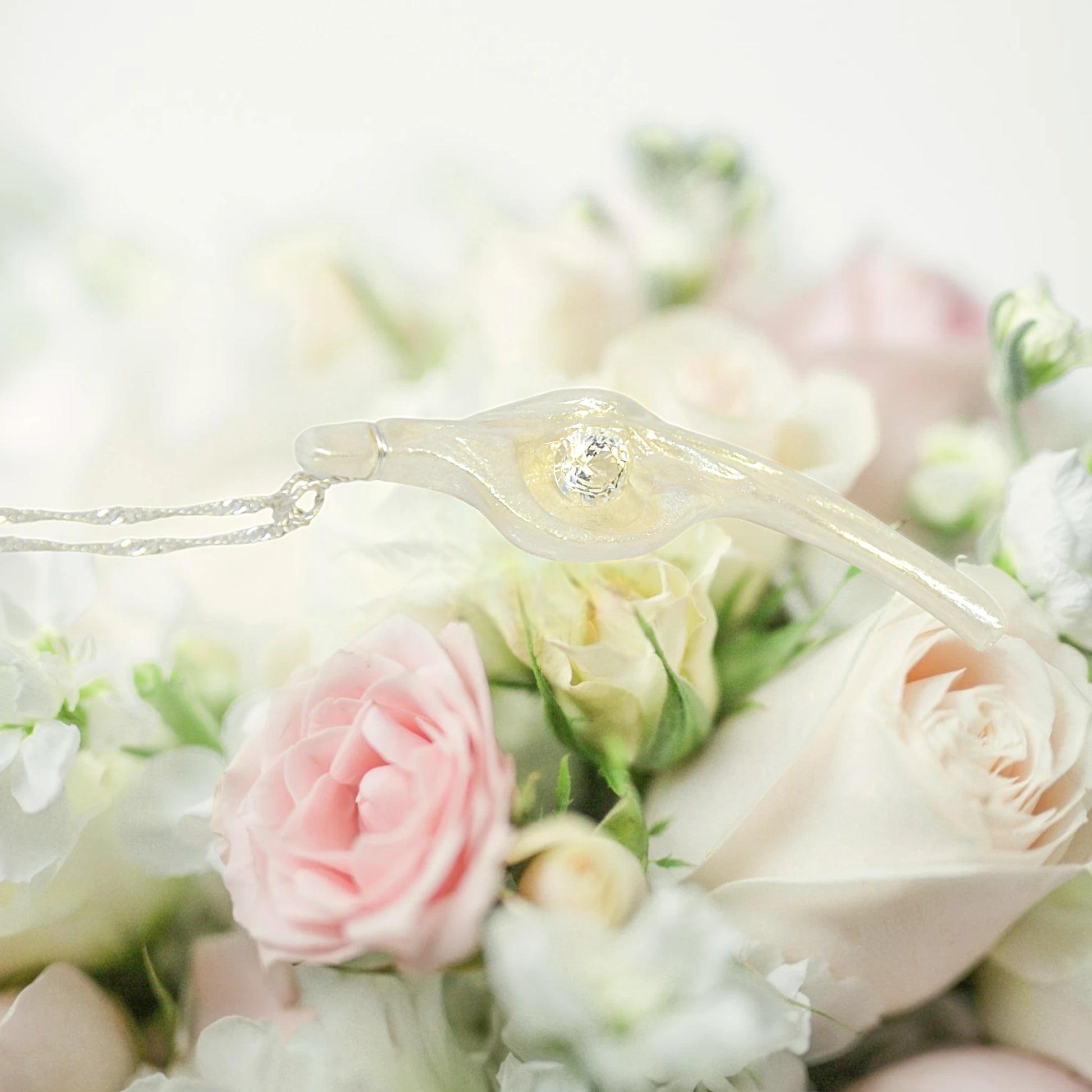 Diamond Star natural seashell pendant with eight mm faceted herkimer diamond. The pendant lays across a bouquet of pink and white roses.