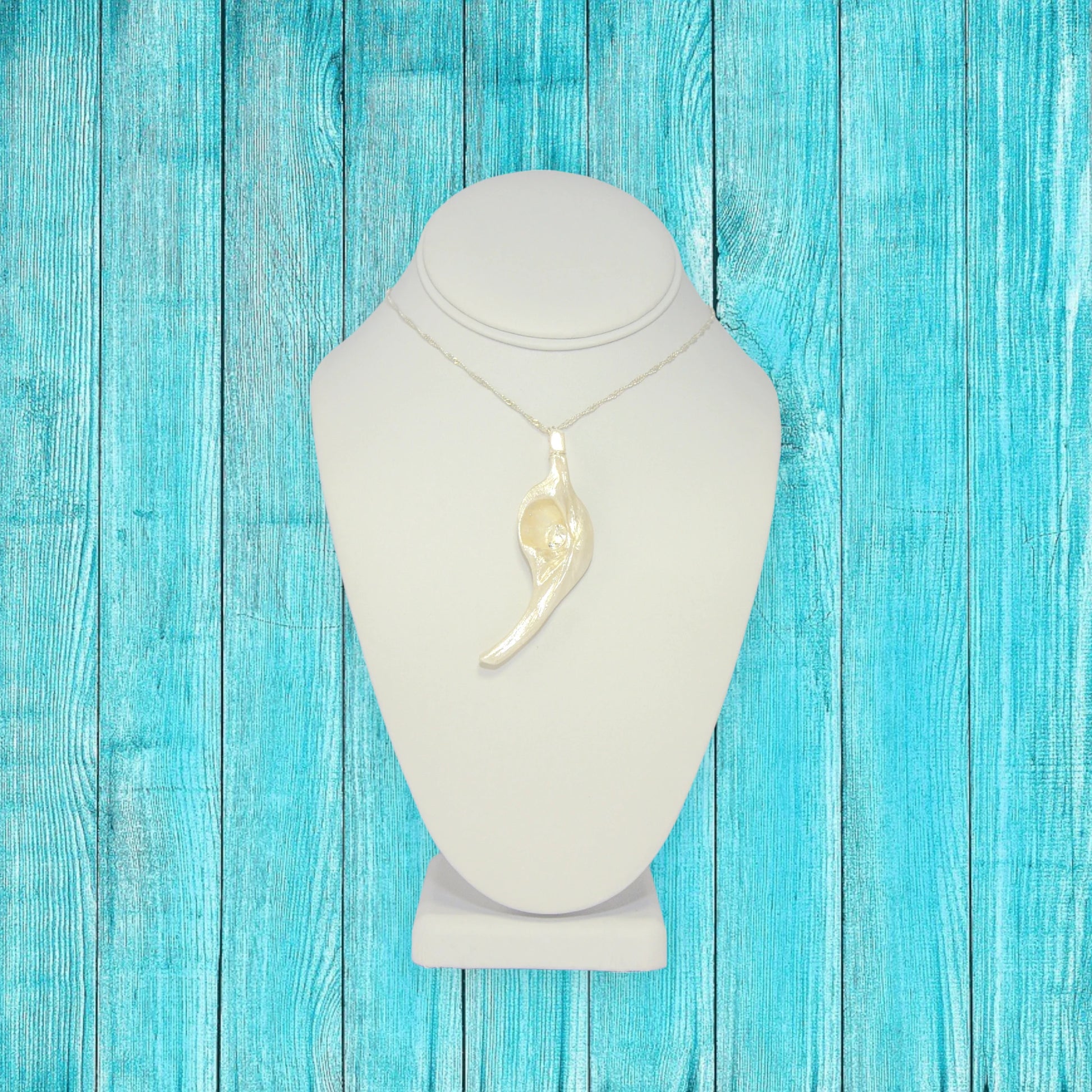 Diamond Star natural seashell pendant with eight mm faceted herkimer diamond. The pendant is hanging on a chain that is on a white necklace displayer. The background is turquoise blue fence boards.