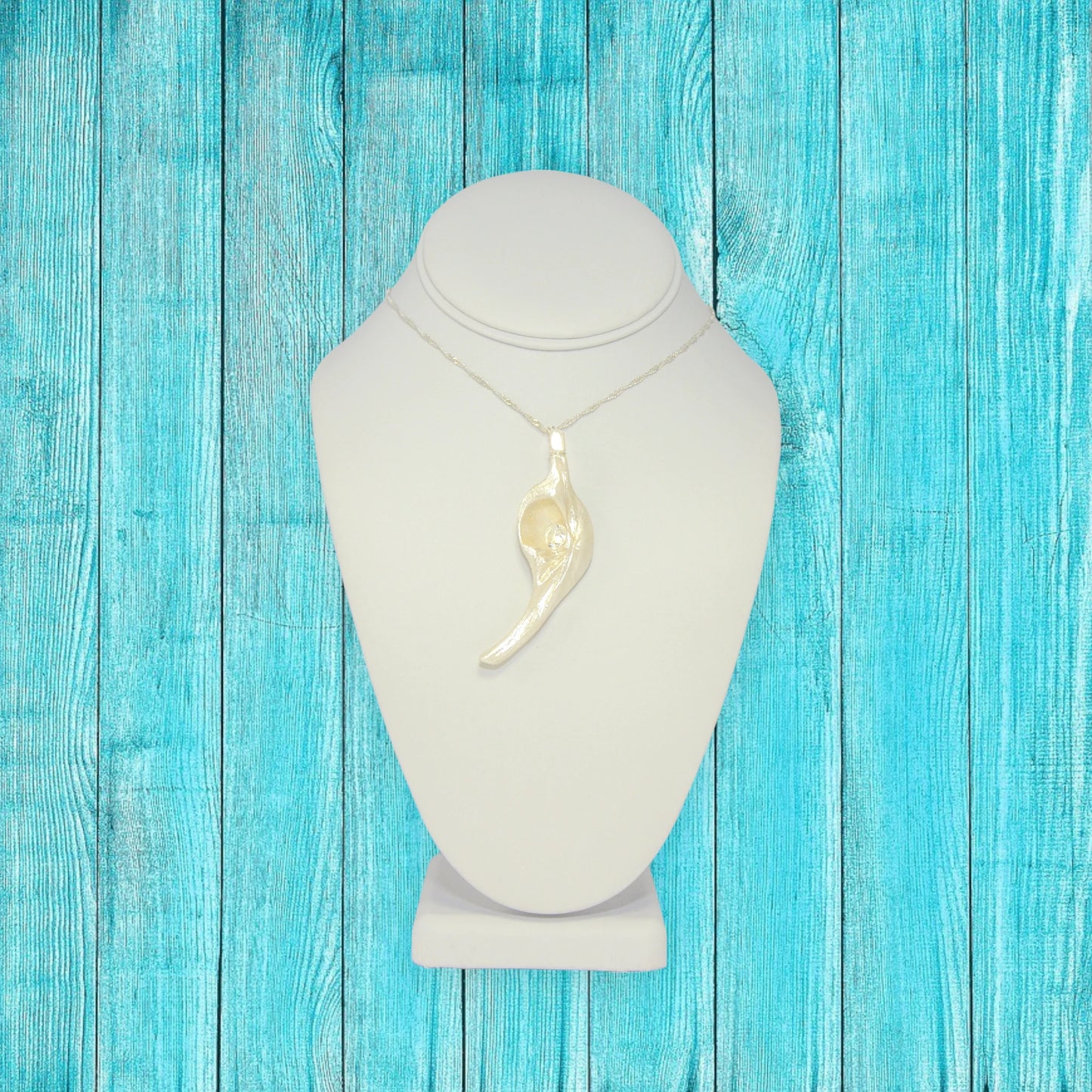 Diamond Star natural seashell pendant with eight mm faceted herkimer diamond. The pendant is hanging on a chain that is on a white necklace displayer. The background is turquoise blue fence boards.