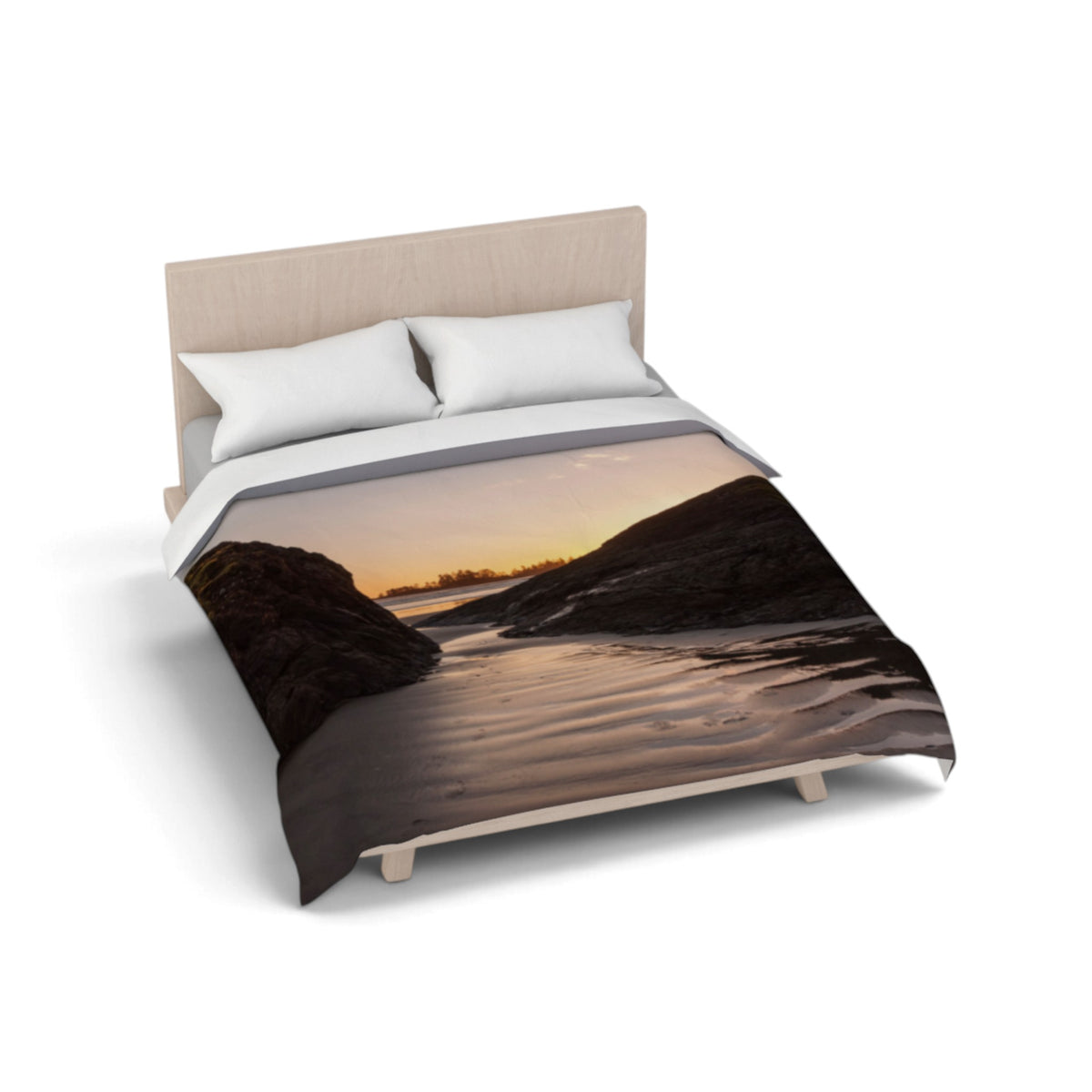 A bed dressed with a duvet cover featuring a scenic landscape print of a rocky shoreline at sunset, styled with two white pillows and a light wood headboard on a white background.