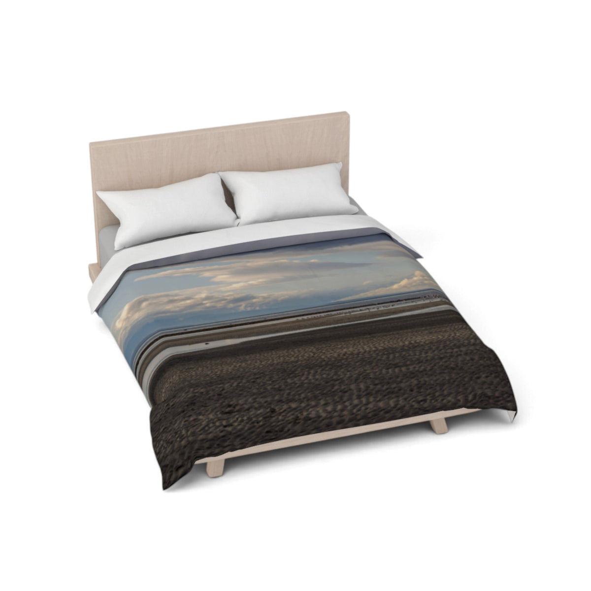 A bed with a duvet cover featuring a landscape print of a beach shoreline under a cloudy sky, styled with two white pillows and a light wood headboard on a white background.