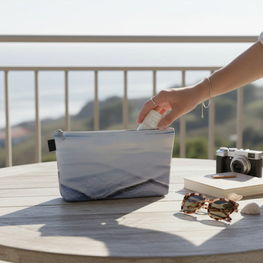 Person reaching into a pouch on a table with sunglasses, camera, and book in the background.