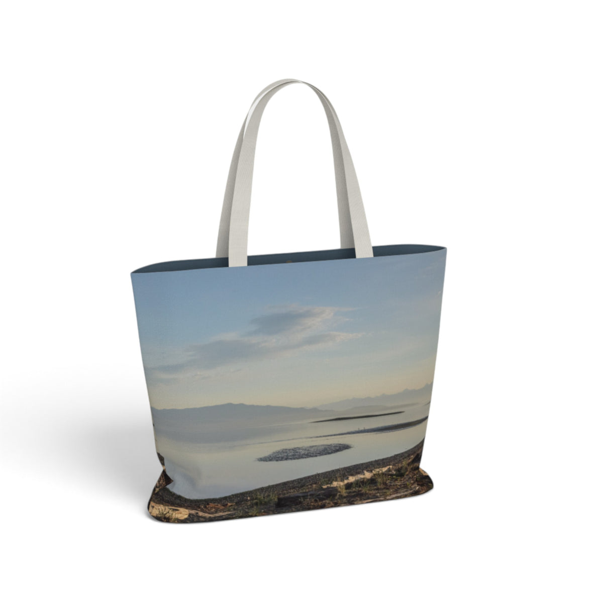 A tote bag featuring a scenic landscape print of a calm lake under a soft blue sky, with white shoulder straps, shown on a clean white background.