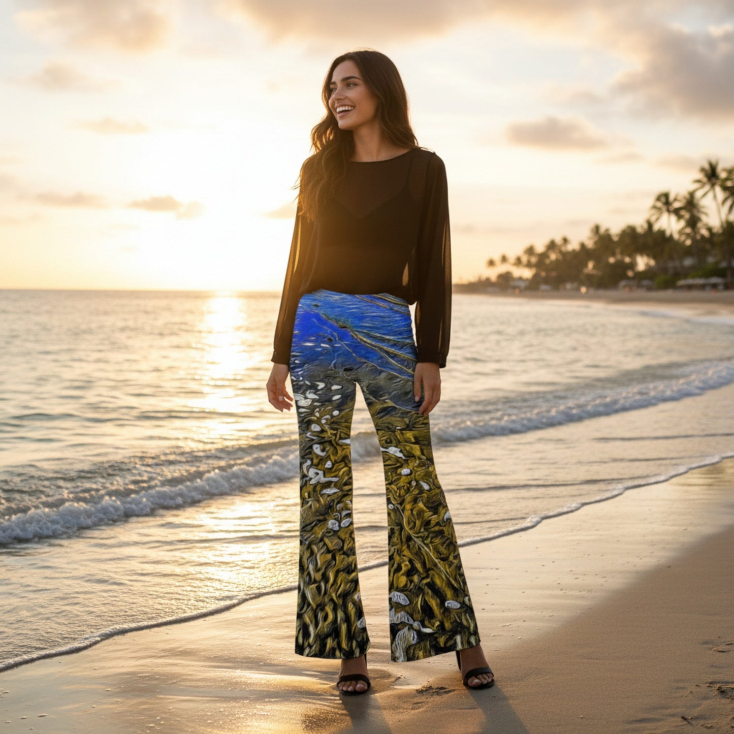 Woman standing on a beach at sunset wearing a black top and patterned pants.