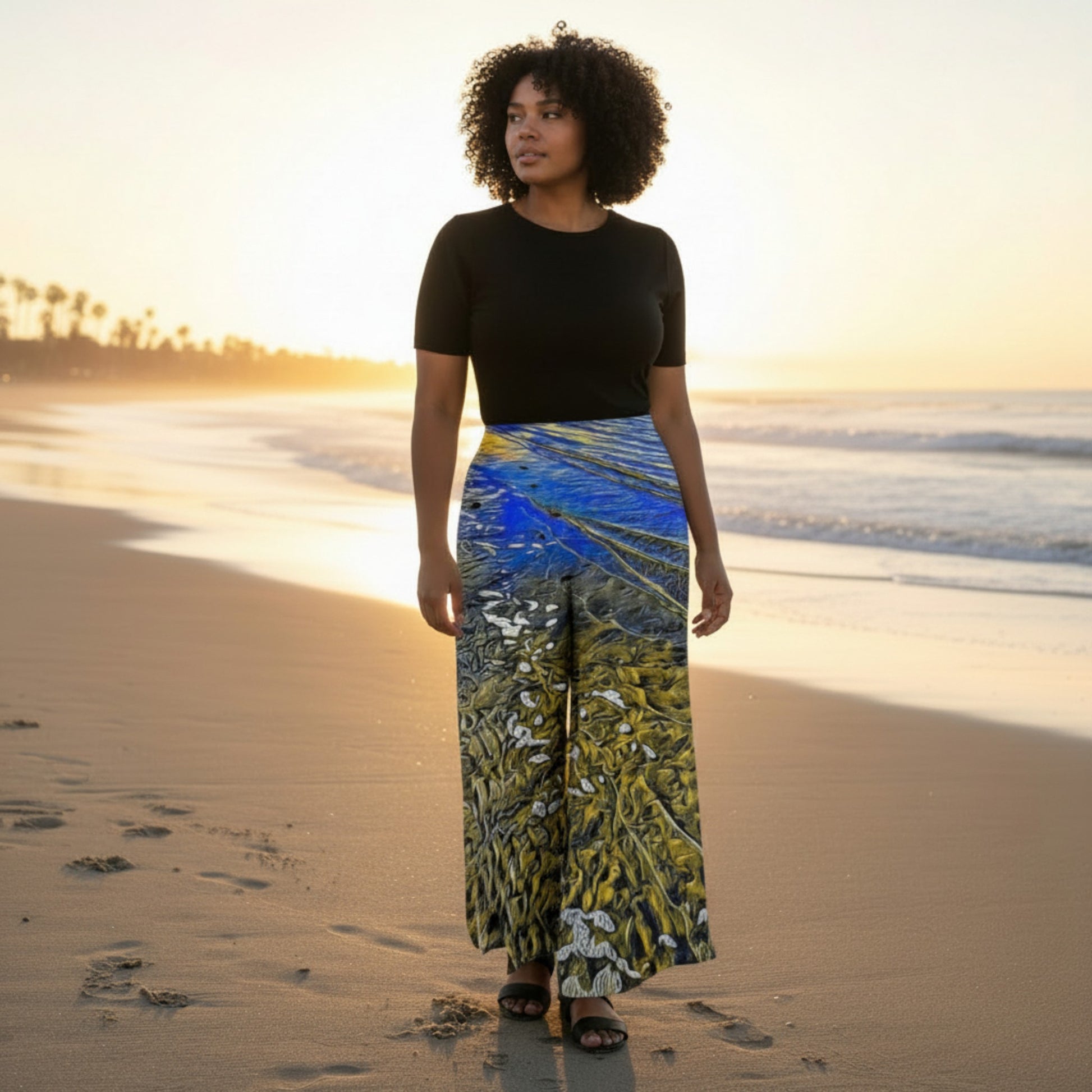 Woman standing on a beach at sunset wearing a black top and colorful skirt.