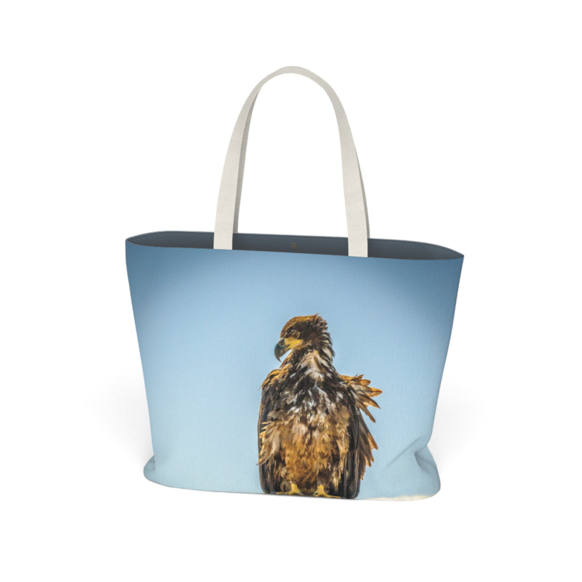 A tote bag with a light blue background and a printed image of a brown eagle on the front, featuring off-white shoulder straps, shown on a plain white background.