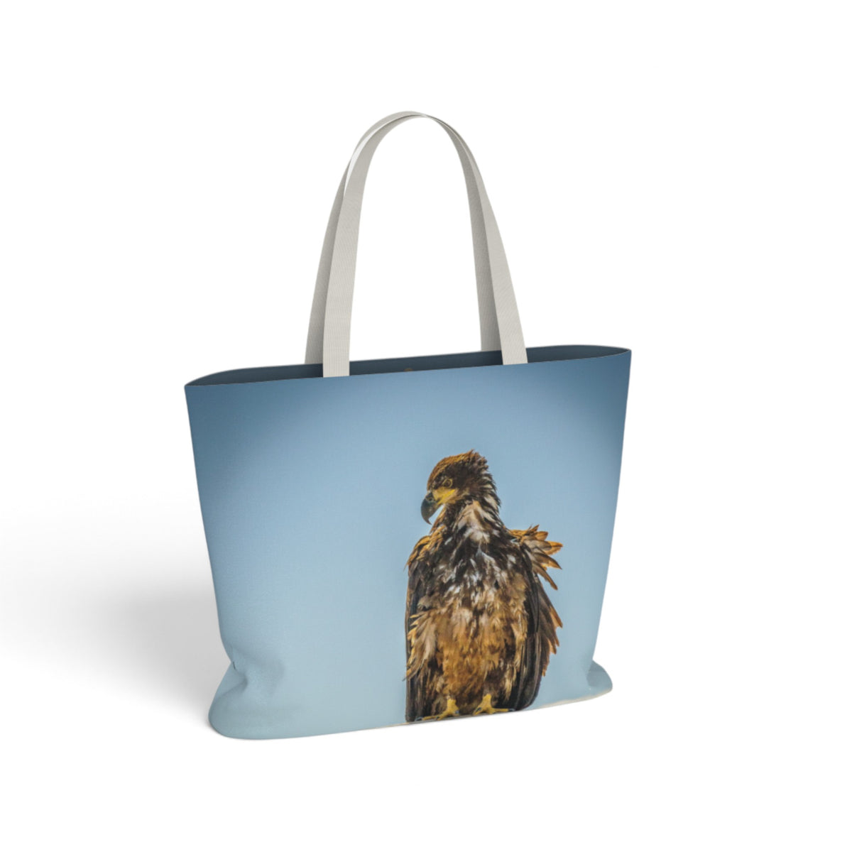 A light blue tote bag with white shoulder straps, featuring a printed graphic of a brown and gold eagle on the front, set against a plain white background.