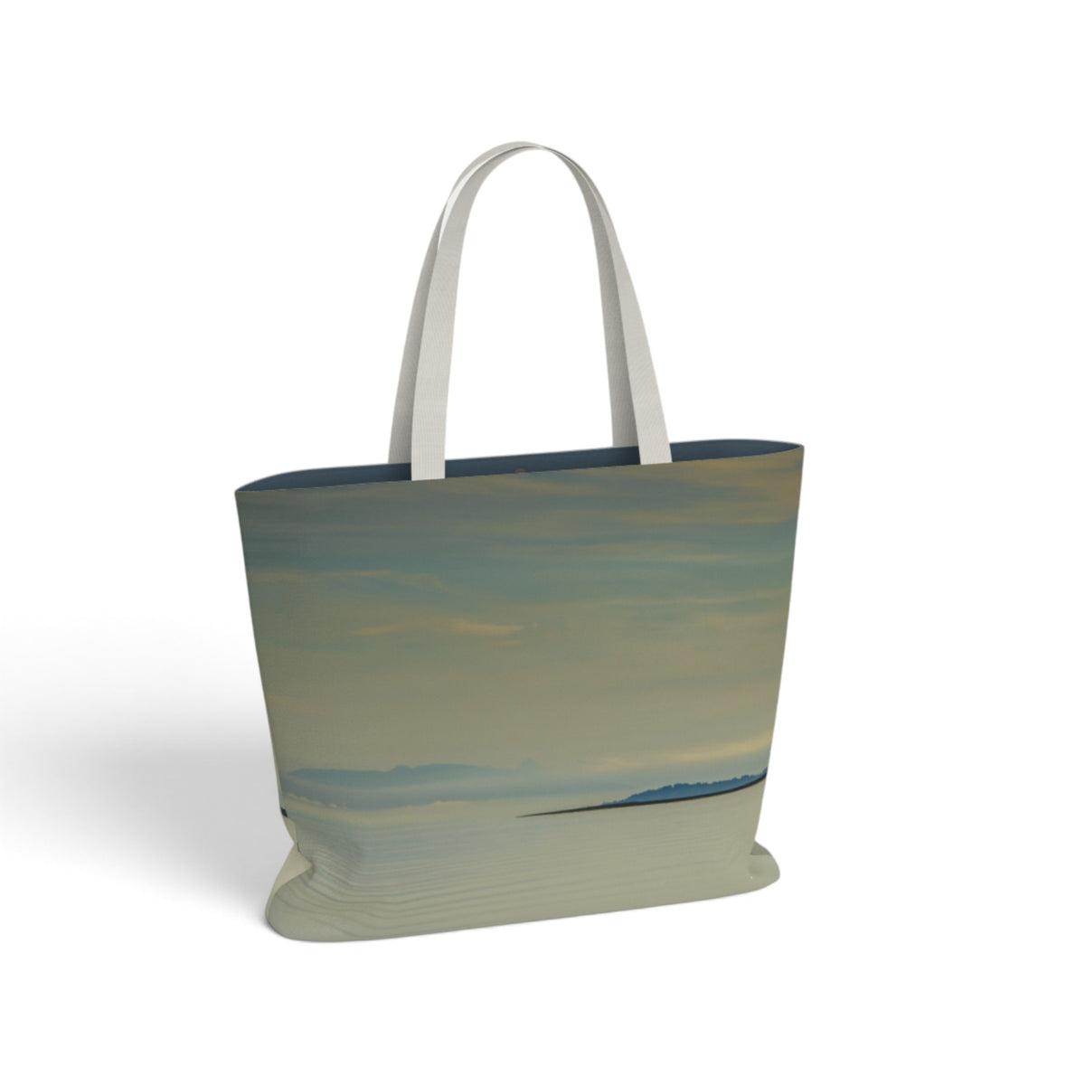 A tote bag featuring a printed landscape design of a beach and sky in muted blue, beige, and gray tones, with solid white shoulder straps, shown on a clean white background.