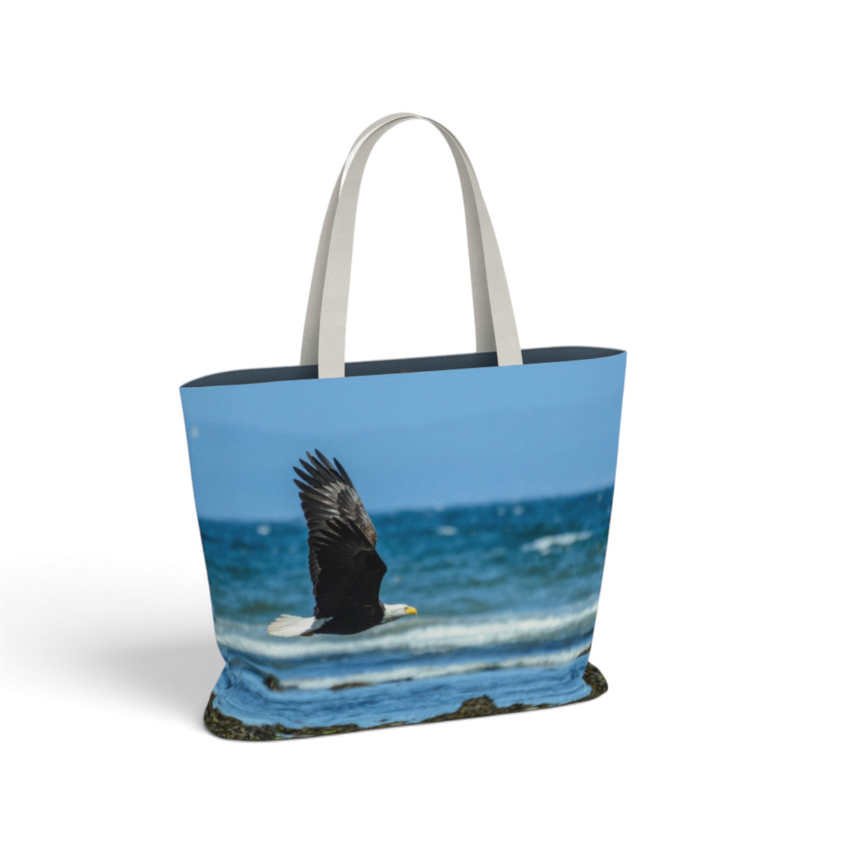 A tote bag featuring a photographic print of a bald eagle flying over blue ocean waves, with light gray fabric handles, shown on a plain white background.