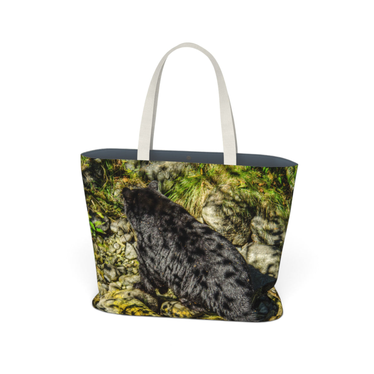 A tote bag featuring a printed photograph of a black bear sitting on mossy rocks, with light beige fabric handles, shown against a plain white background.