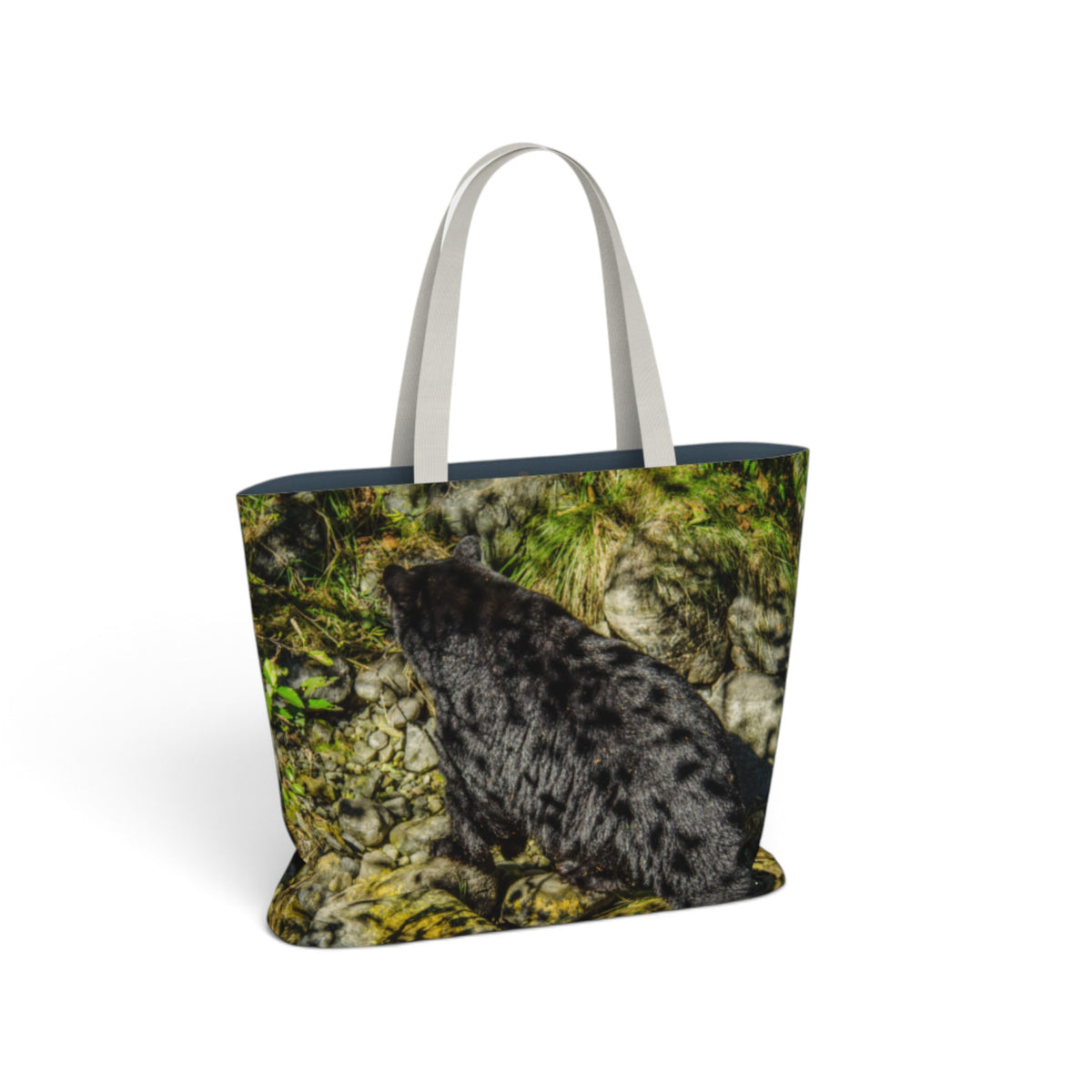 A tote bag featuring a printed photograph of a black bear on a mossy rock, with light gray fabric handles, shown on a plain white background.