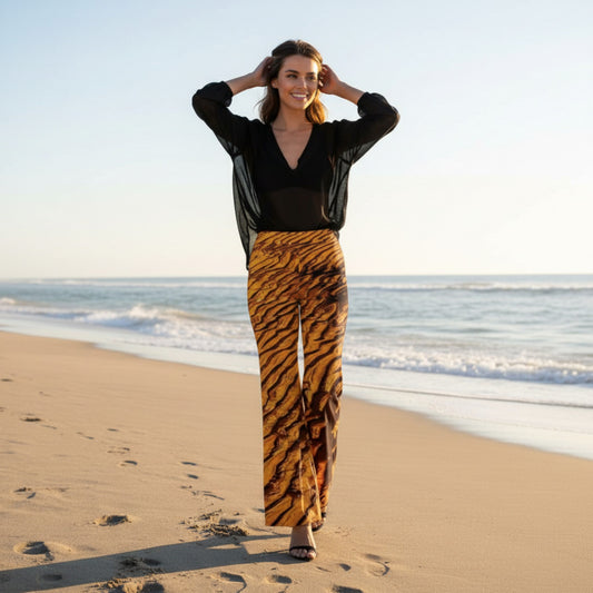 Woman wearing a black top and sand design pants standing on a beach.