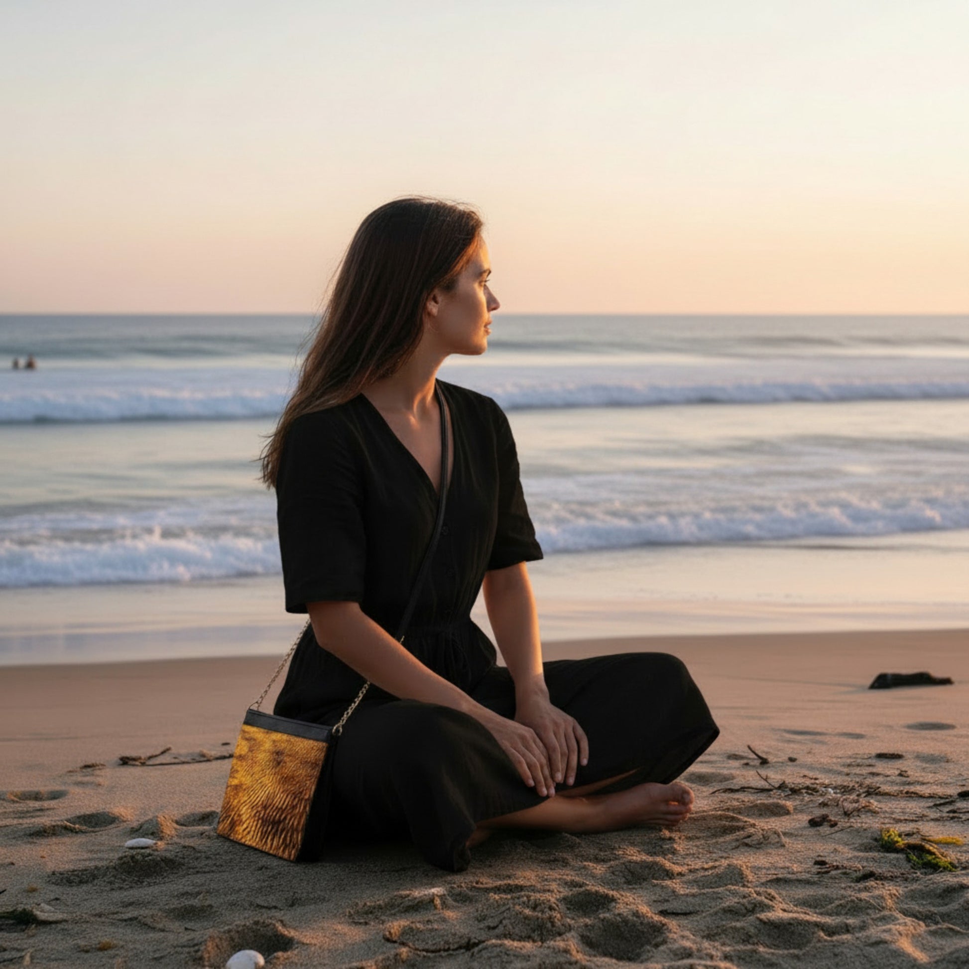 Woman sitting on the beach at sunset with a bag by her side.