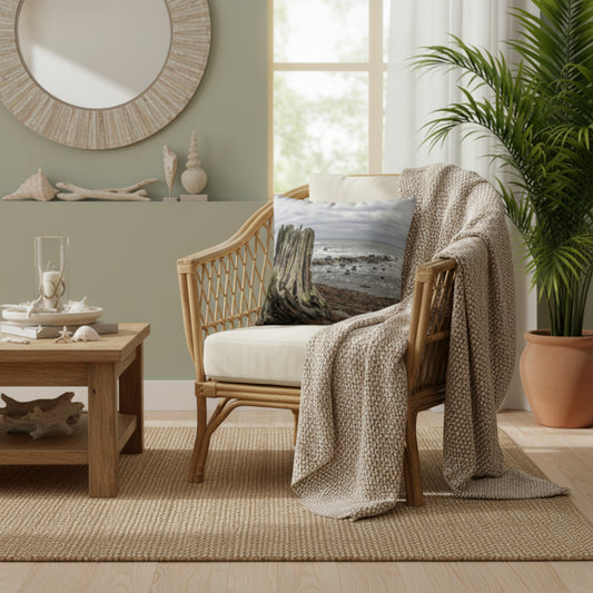 Beach themed pillow a rattan chair with a throw blanket draped over the arm of the chair.