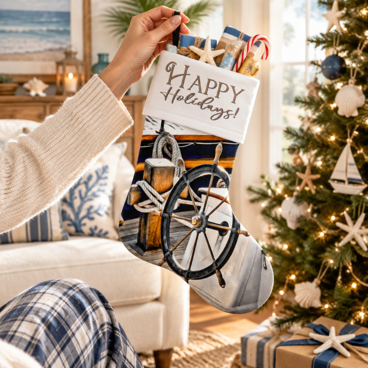 A person holds a Christmas stocking decorated with a nautical ship's wheel, rope, wooden dock, and a white patch reading 'Happy Holidays!' in a cozy living room by a decorated Christmas tree.