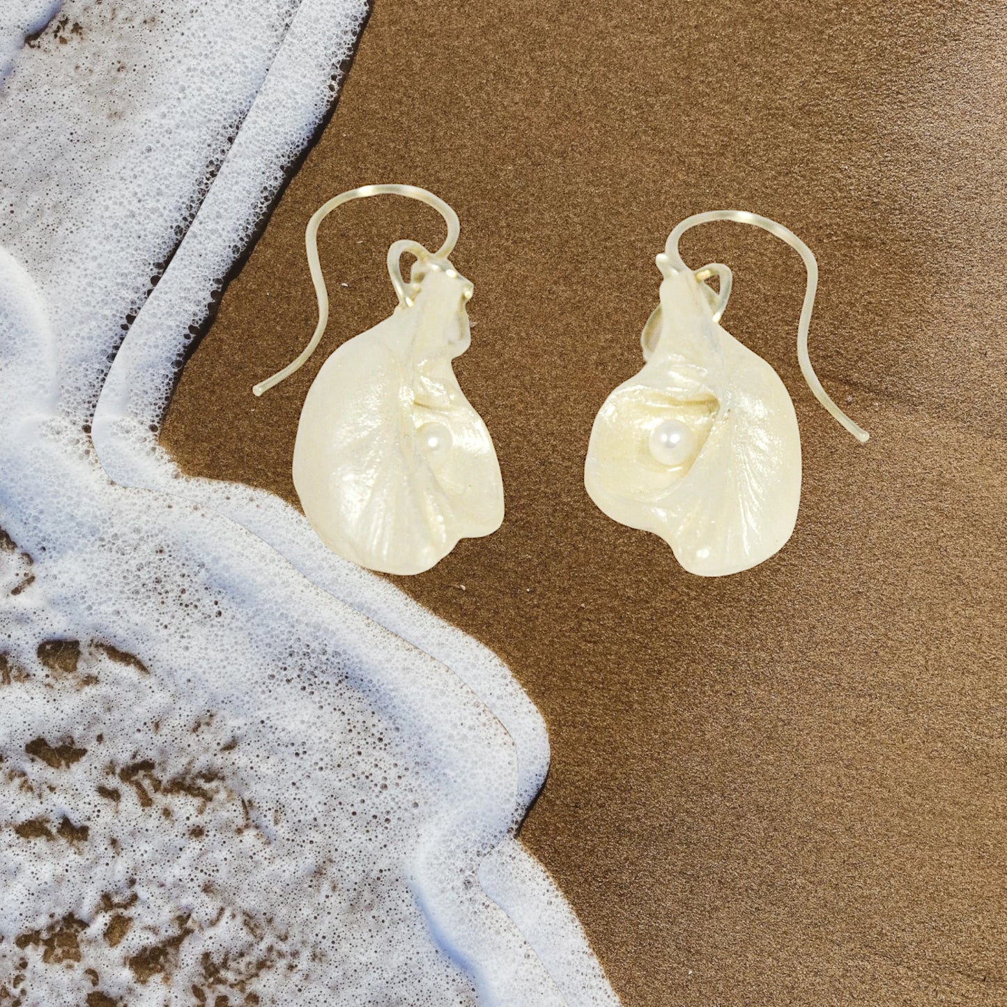 Harmony Earrings made of natural seashells and real freshwater pearls.  The earrings are shown laying on the sand ocean wave.