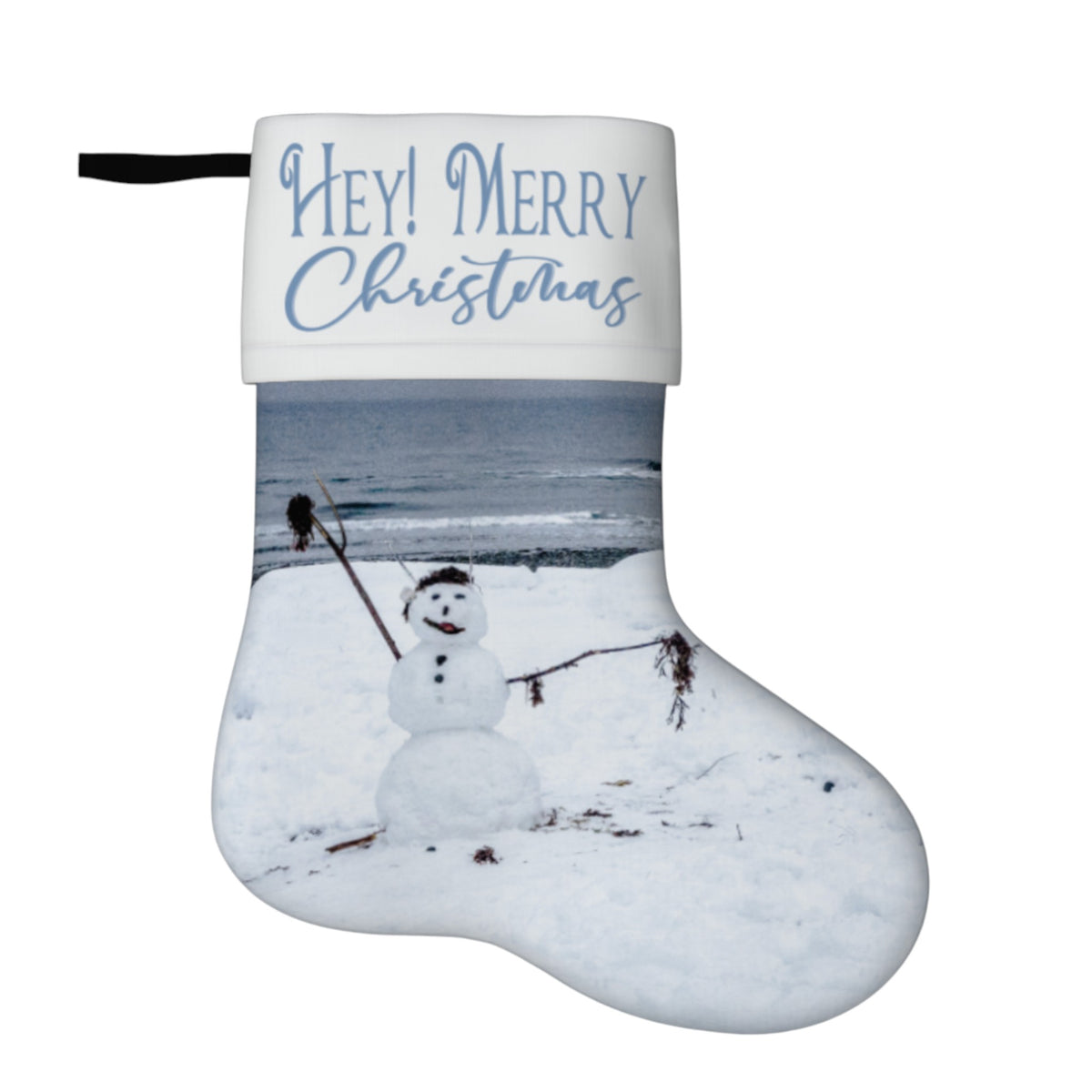 A Christmas stocking with a white cuff printed with 'HEY! MERRY Christmas' in blue script, and the rest of the stocking featuring a winter scene of a snowman in a snowy landscape by the sea.