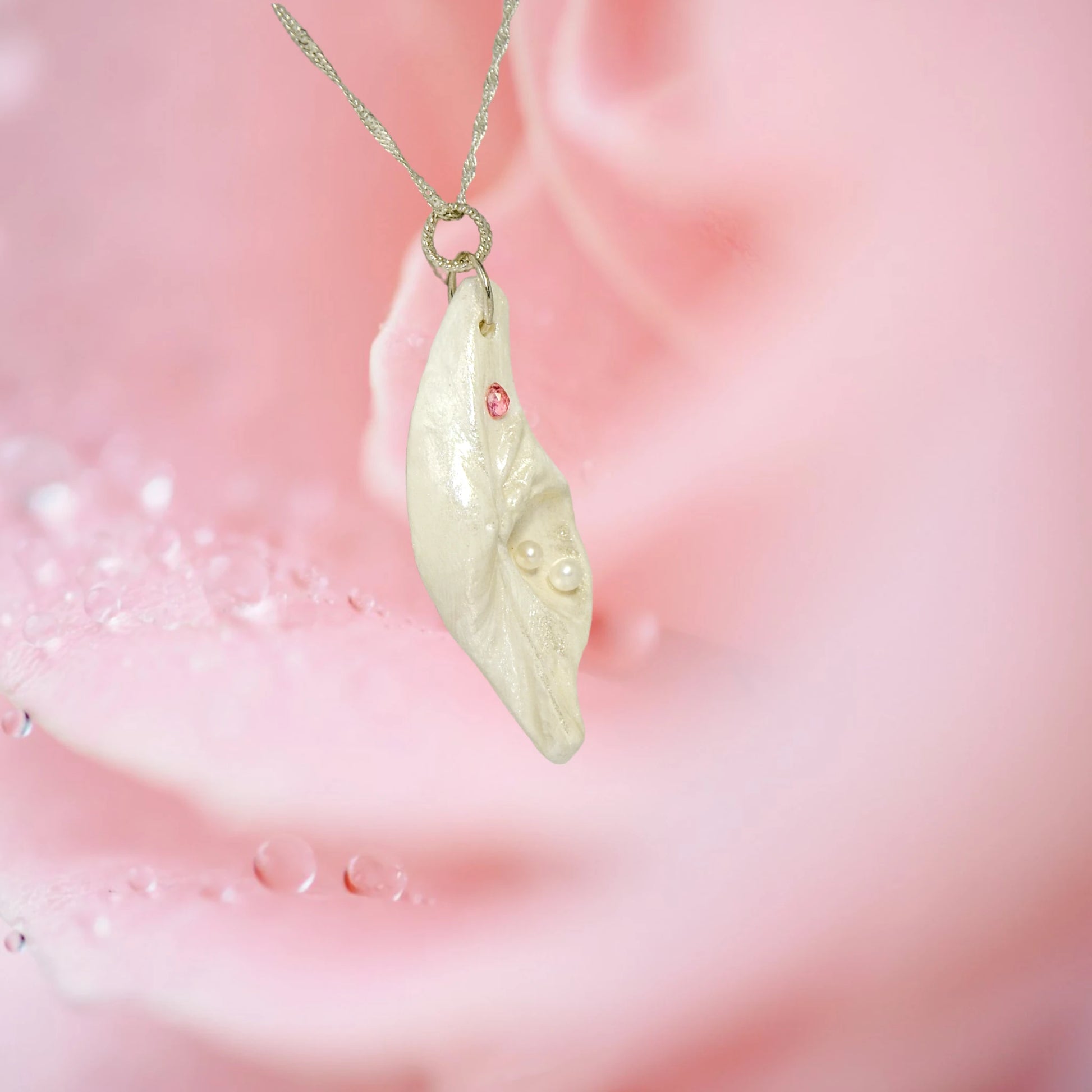 A trio of white baby freshwater pearls and a teardrop rose cut pink tourmaline gemstone compliments the seashell pendant beautifully. The pendant is turned so the viewer can see the right side of the pendant.