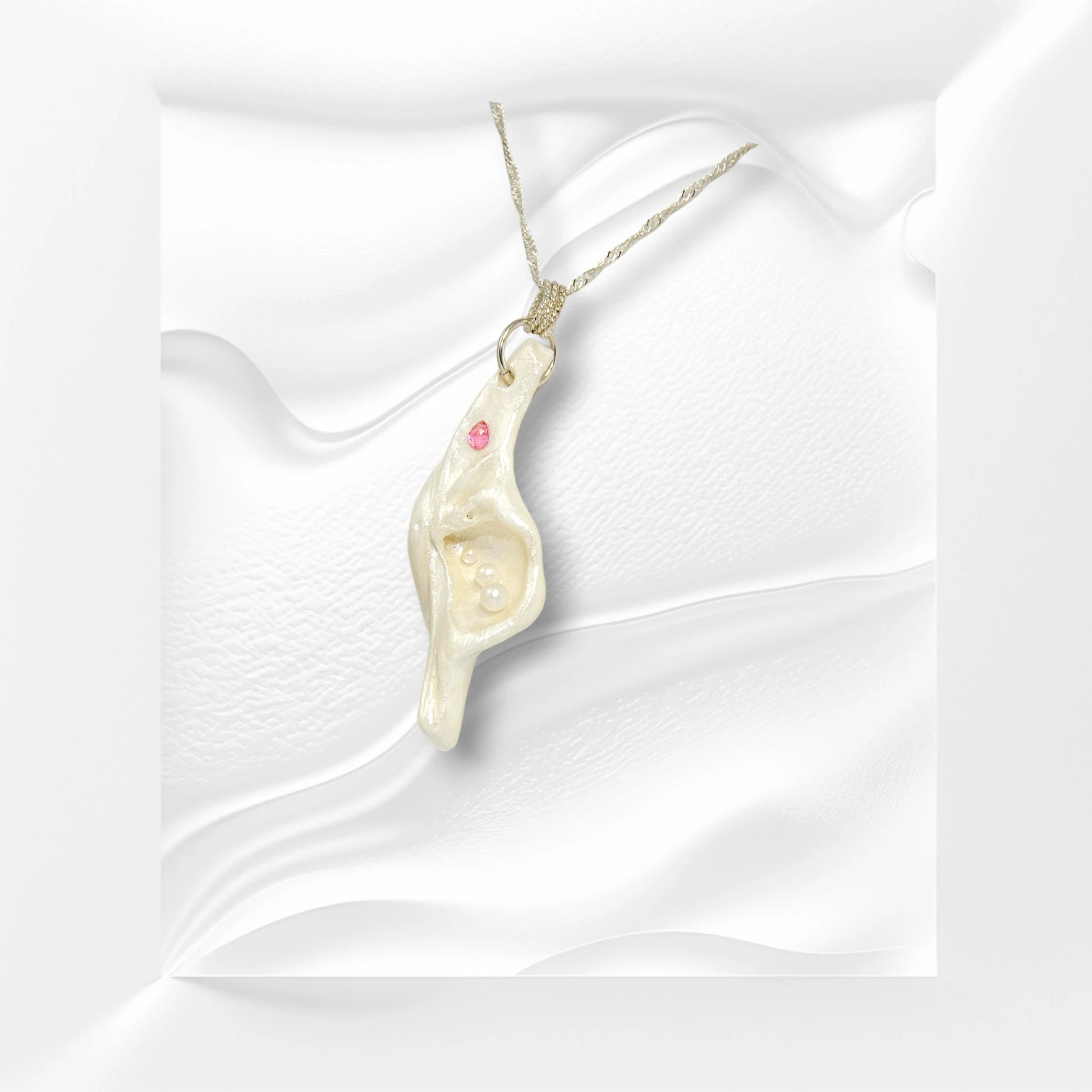 A trio of white baby freshwater pearls and a teardrop rose cut pink tourmaline gemstone compliments the seashell pendant beautifully. The pendant is turned to the viewer can see the right side of the pendant.