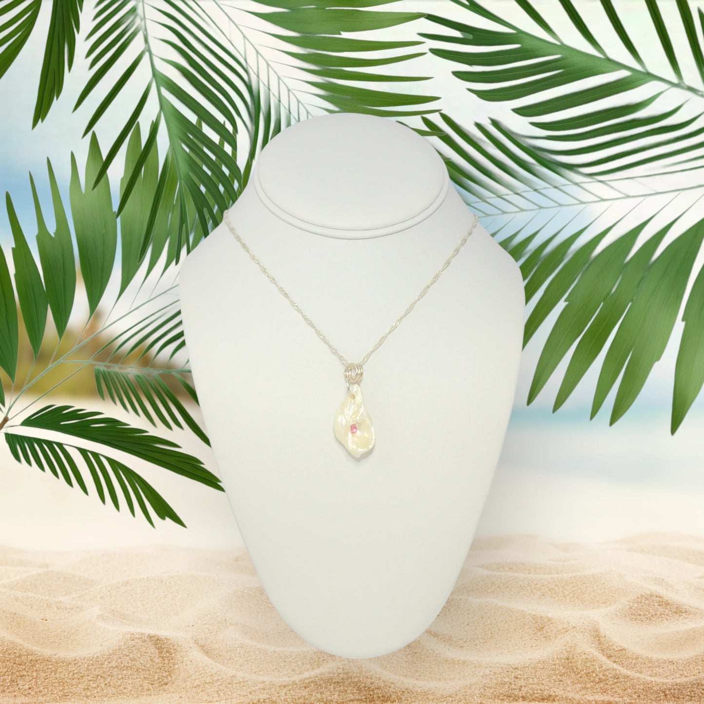 Jewel natural seashell with a real teardrop shaped rose cut pink tourmaline gemstone compliments the pendant. The pendant is shown hanging on a white necklace displayer with a beach background.