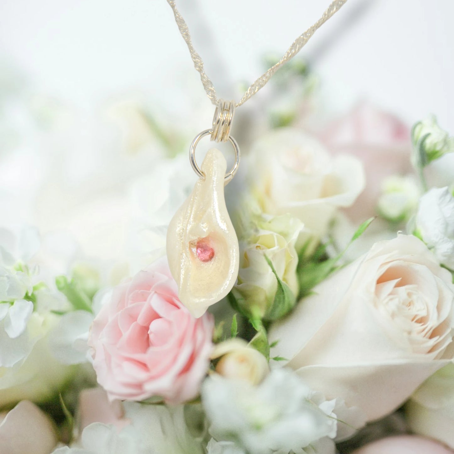 Jewel natural seashell with a real teardrop shaped rose cut pink tourmaline gemstone compliments the pendant. The pendant is hanging over a bouquet of pink and white roses.