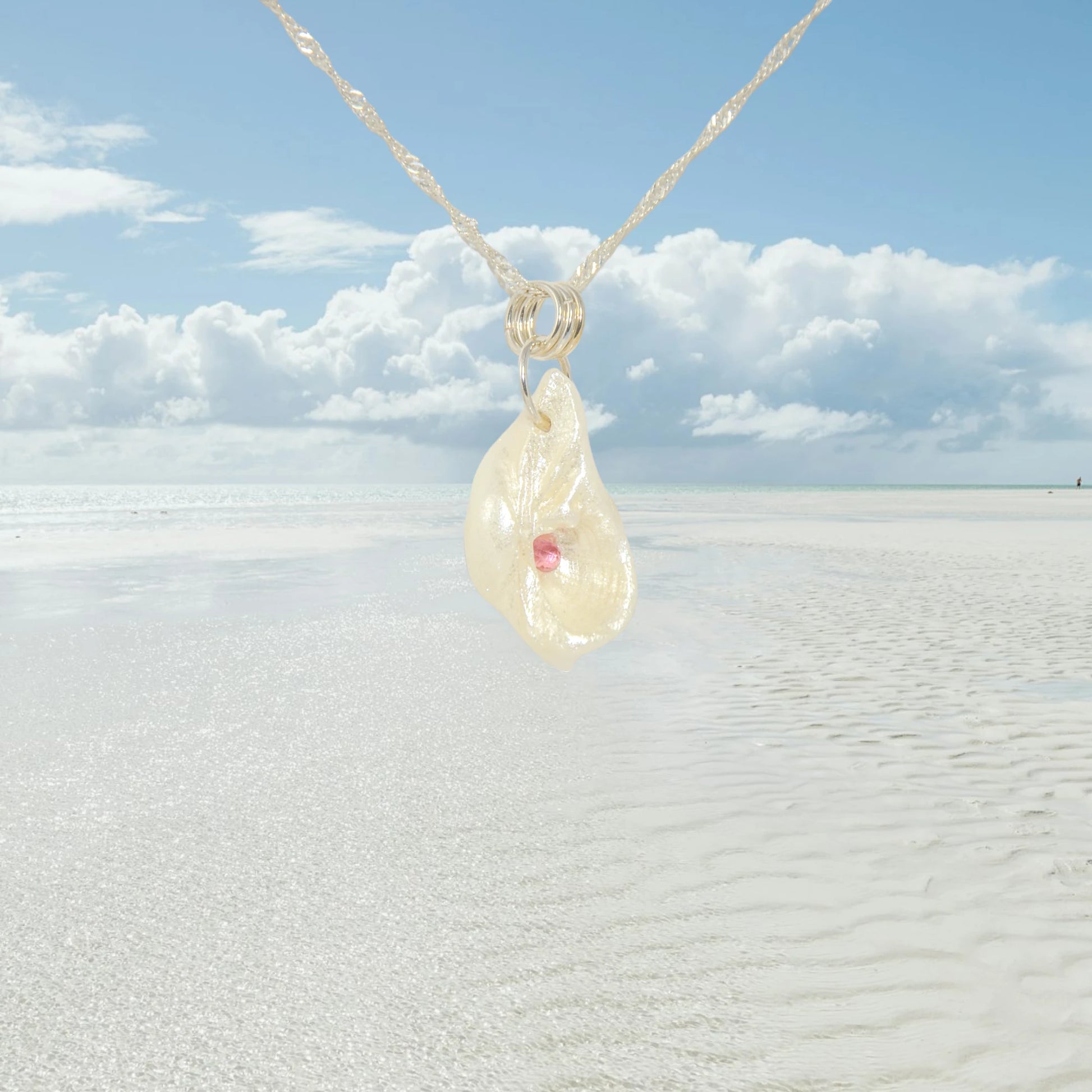 Jewel natural seashell with a real teardrop shaped rose cut pink tourmaline gemstone compliments the pendant. The background shows a ocean with clouds in the background.