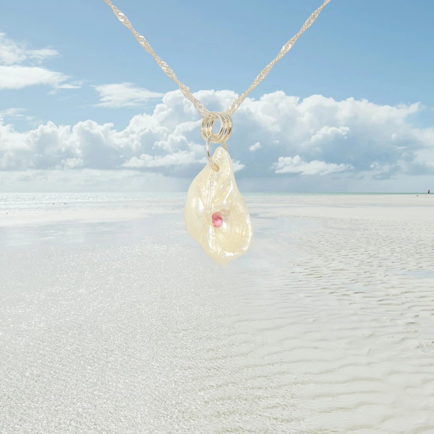 Jewel natural seashell with a real teardrop shaped rose cut pink tourmaline gemstone compliments the pendant. The background shows a ocean with clouds in the background.