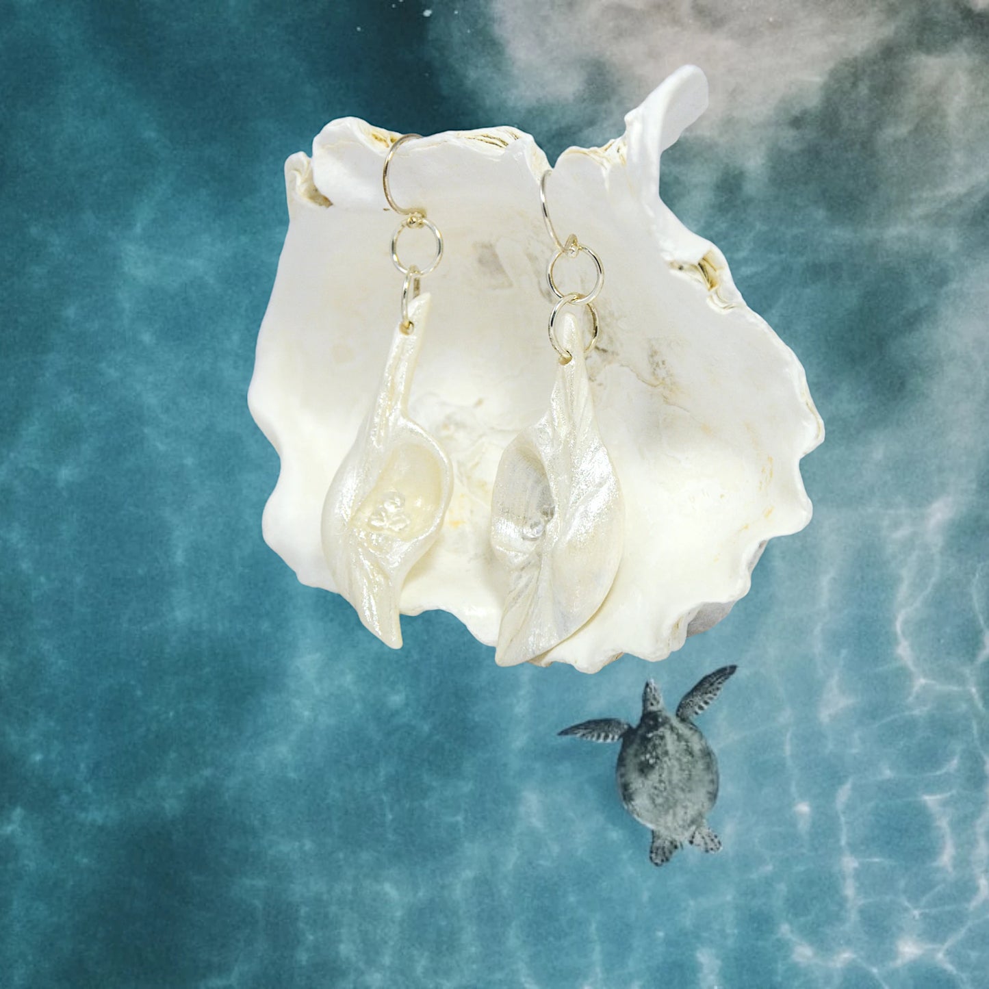 Dream Stone natural seashell earrings with herkimer diamonds. The earrings are shown hanging from a larger seashell and the ocean background has a turtle swimming in it.