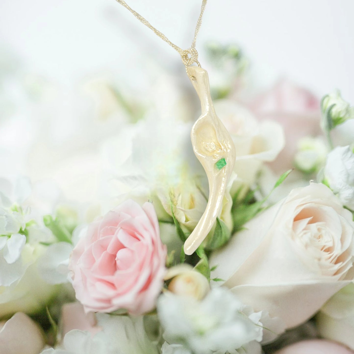 Empress natural seashell pendant with a Herkimer Diamond and Emerald. The pendant hangs from a chain over a bouquet of pink and white roses.