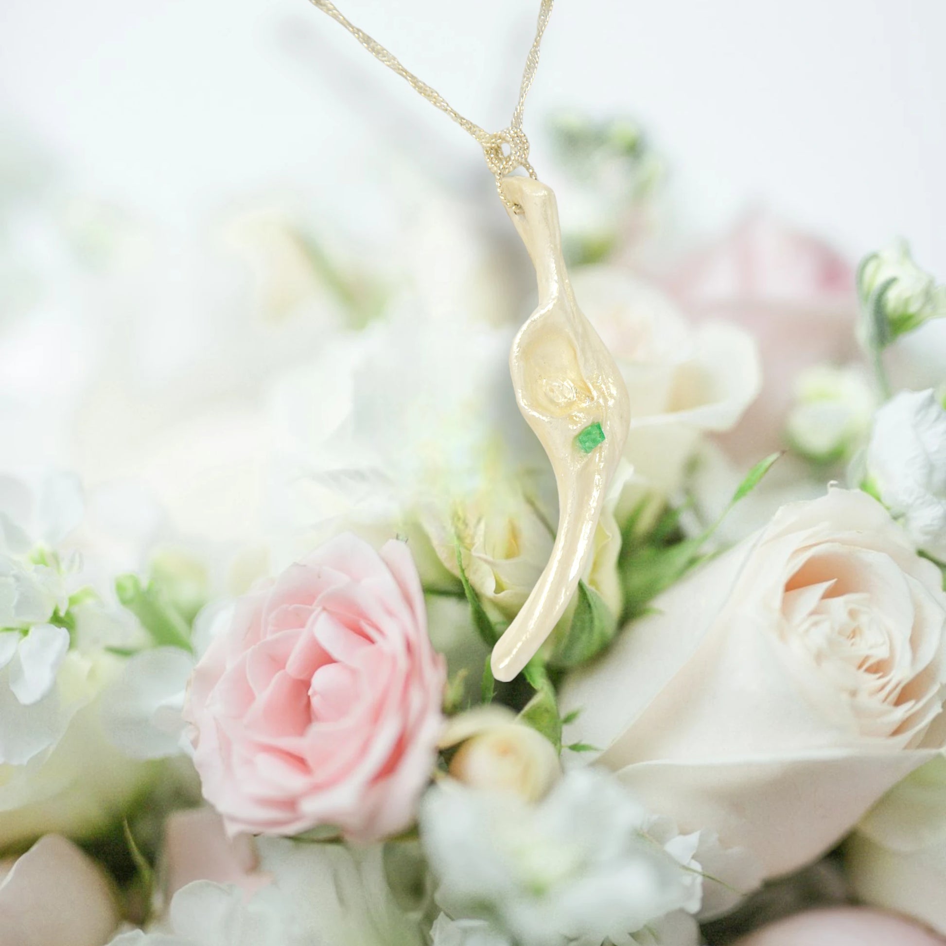 Empress natural seashell pendant with a Herkimer Diamond and Emerald. The pendant hangs from a chain over a bouquet of pink and white roses.