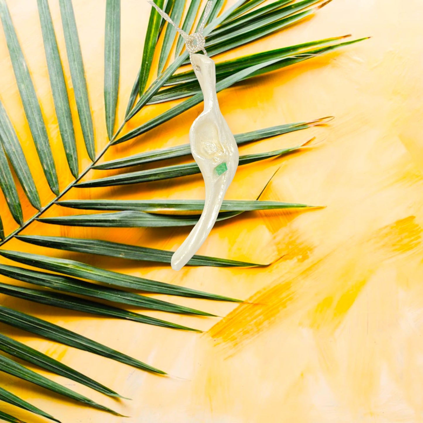 Empress natural seashell pendant with a Herkimer Diamond and Emerald. The background is a palm frond on a yellow background.