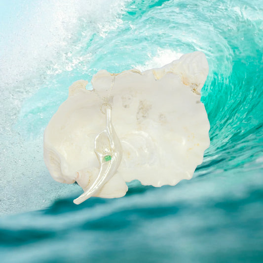 Empress natural seashell pendant with a Herkimer Diamond and Emerald. The pendant hangs from a larger seashell with an ocean wave in the background.