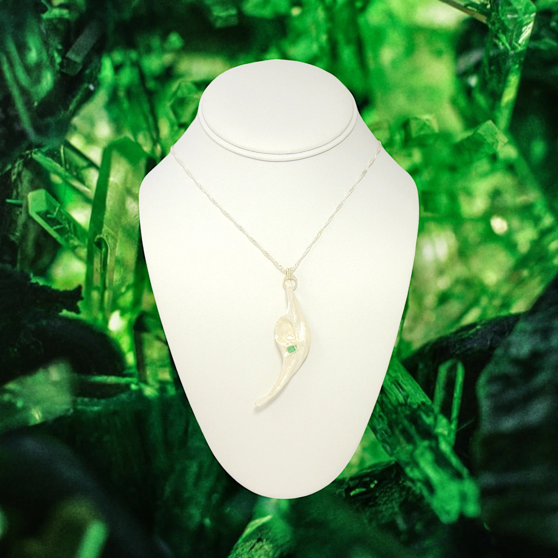 Empress natural seashell pendant with a Herkimer Diamond and Emerald. The pendant is hanging from a chain on a white necklace displayer with emerald gemstones in the background.