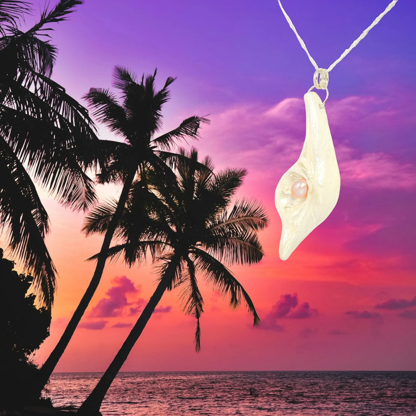 The pendant Champagne on Ice is shown hanging by a necklace with a beautiful purple magenta pink sunset with palm trees  and the ocean.  Summer Vibes