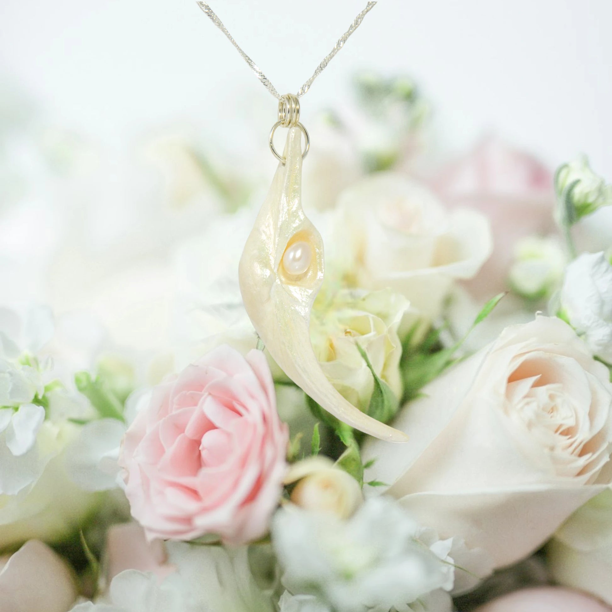Jupiter is a natural seashell pendant with a real freshwater pearl. The pendant is shown hanging over a bouquet of pink and white roses.
