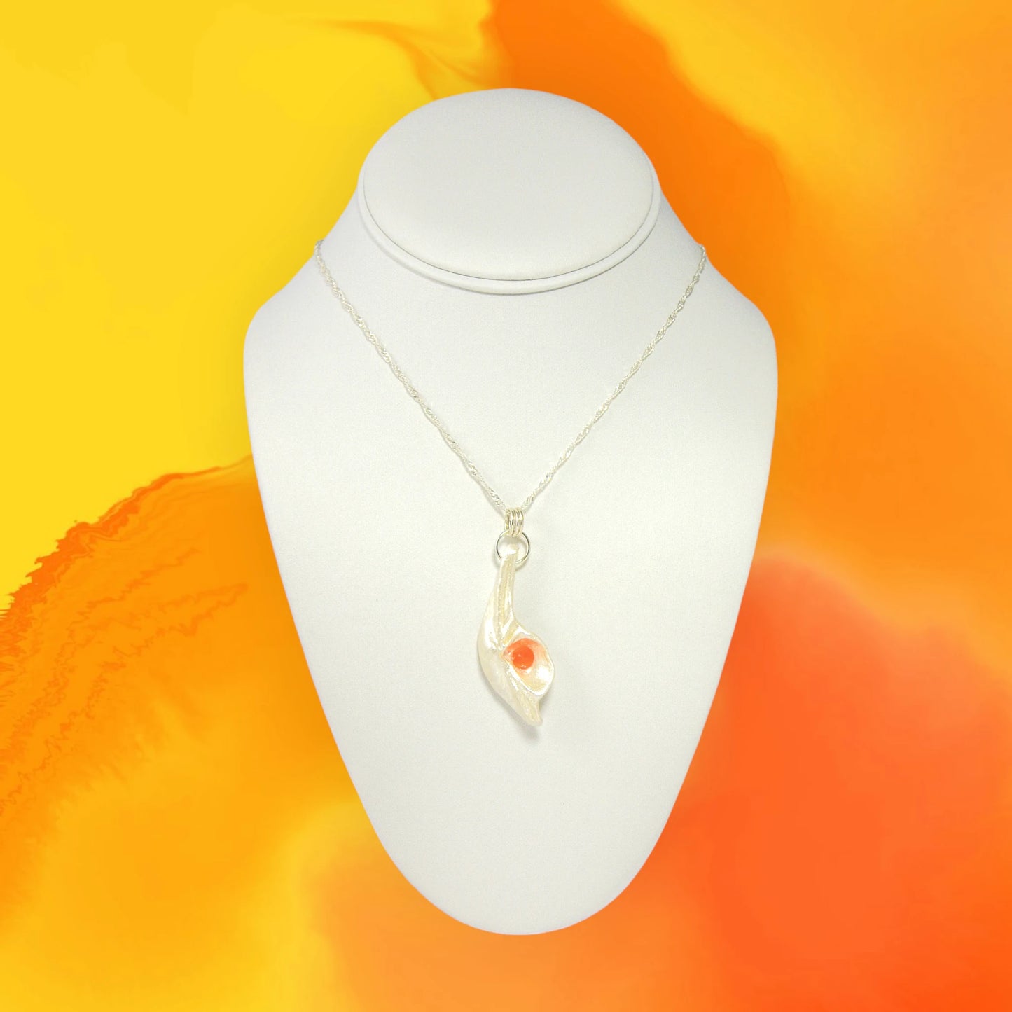 Natural Seashell pendant, elevating the beautiful natural nuances to new heights. The pendant is perfectly adorned with a mesmerizing rose cut Carnelian gemstone. The pendant is hanging on a necklace over a white displayer.  the background is orange and yellow.