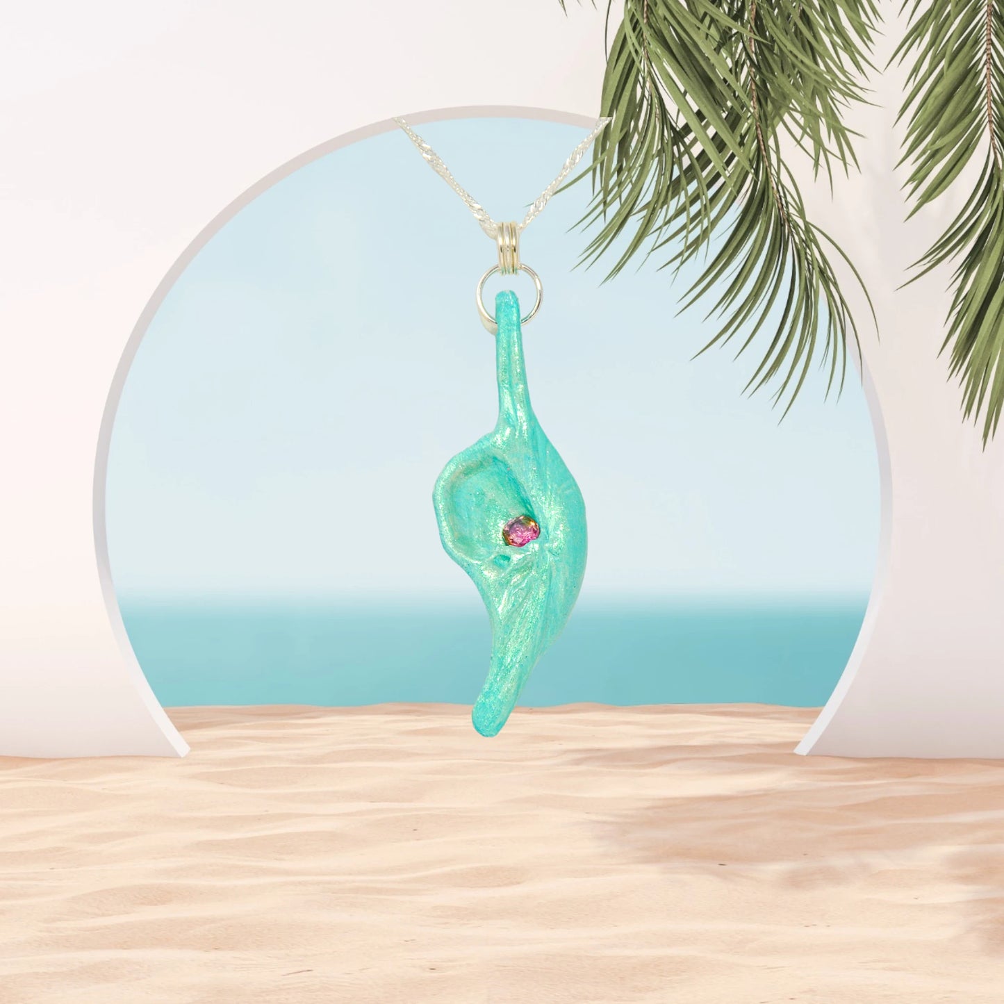 Rio is a natural seashell pendant with a faceted Pink Tourmaline gemstone. The pendant is shown hanging in an archway leading to the ocean.