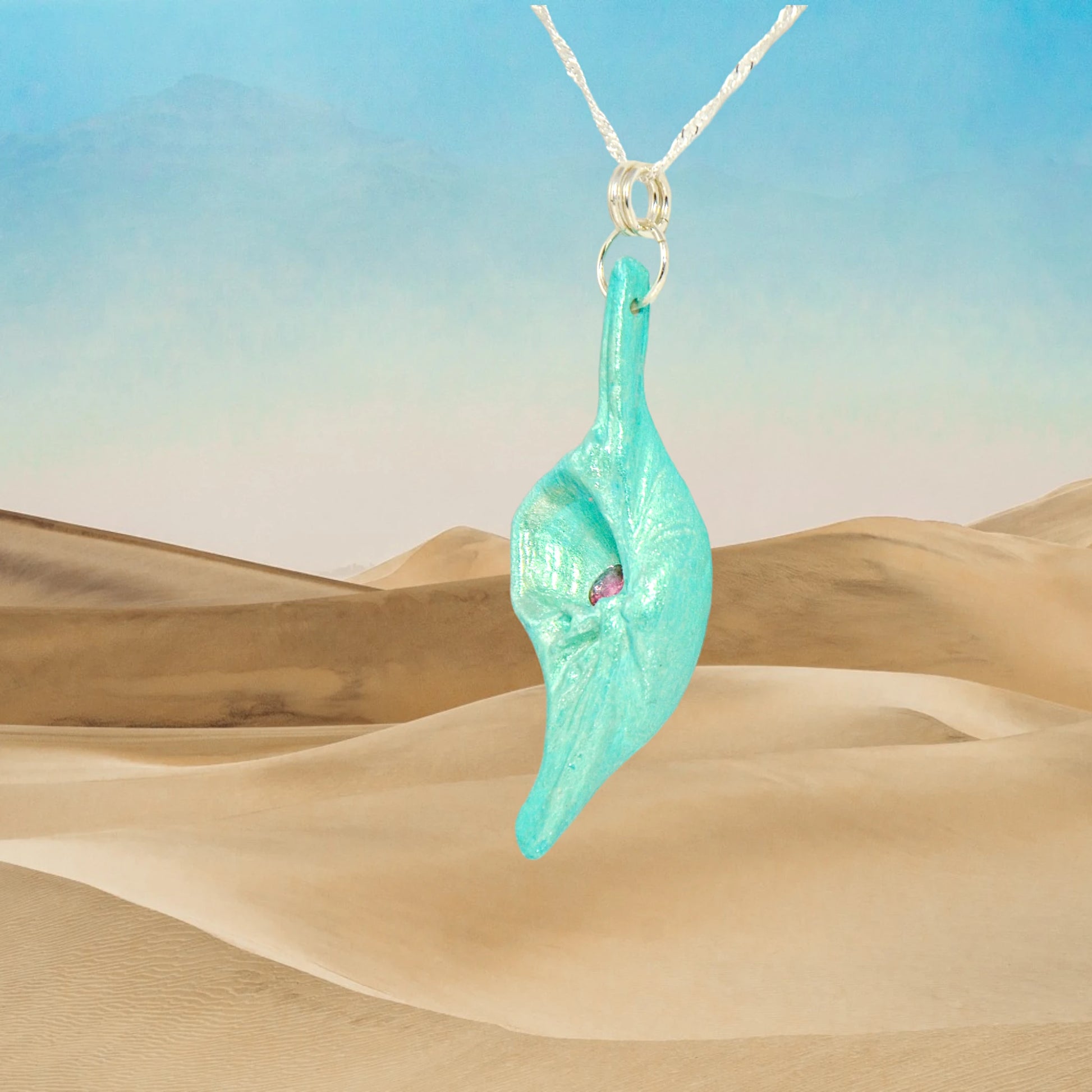 Rio is a natural seashell pendant with a faceted Pink Tourmaline gemstone.  The background is of sand dunes.